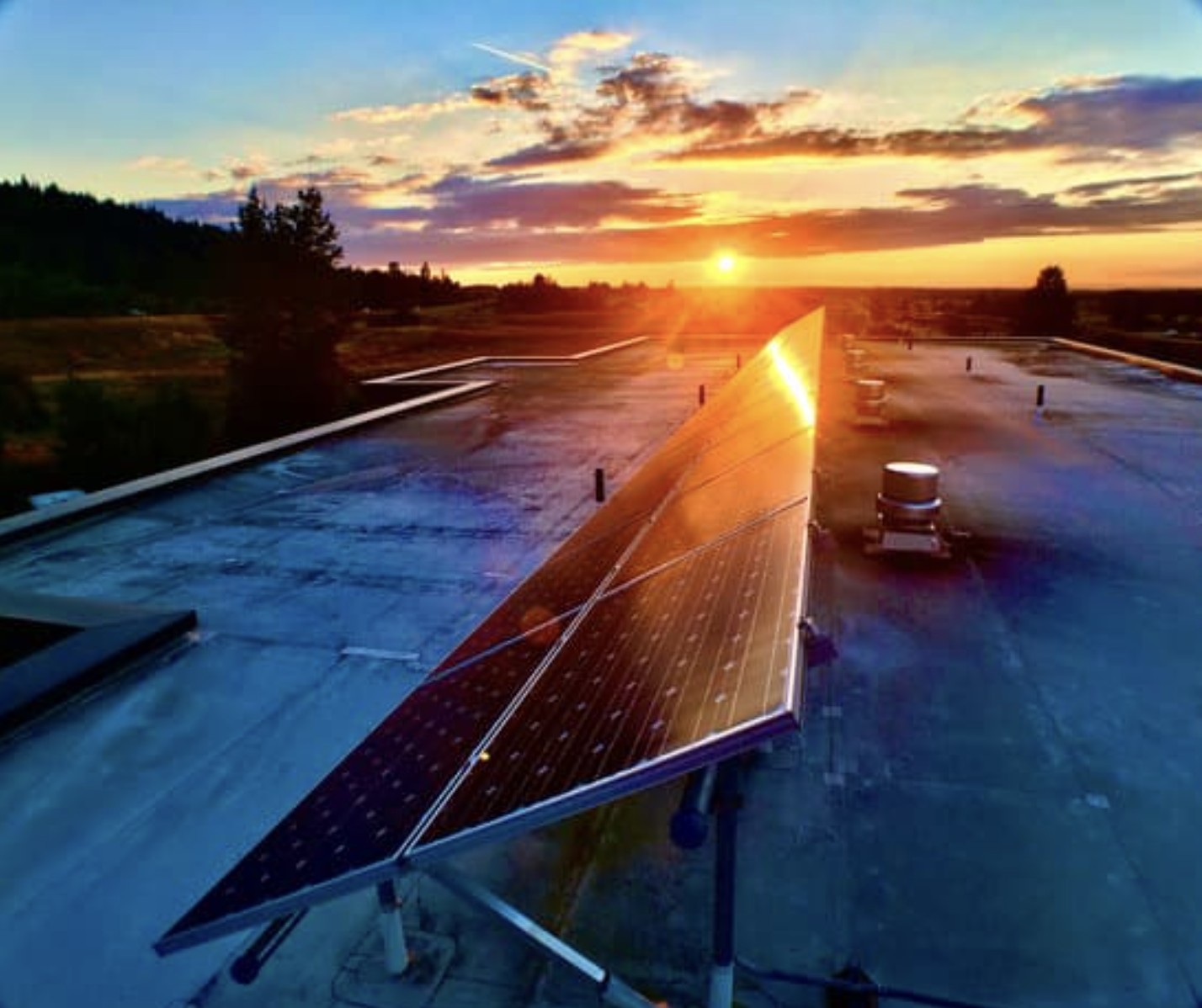 Solar panels installed on a rooftop at sunset with a scenic landscape and colorful sky in the background.