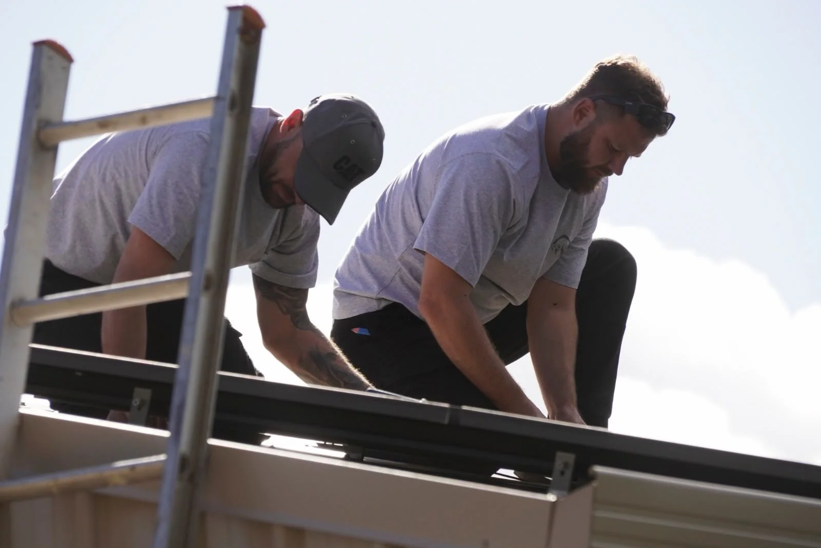 A worker installing solar panels on a rooftop under a blue sky with clouds.
