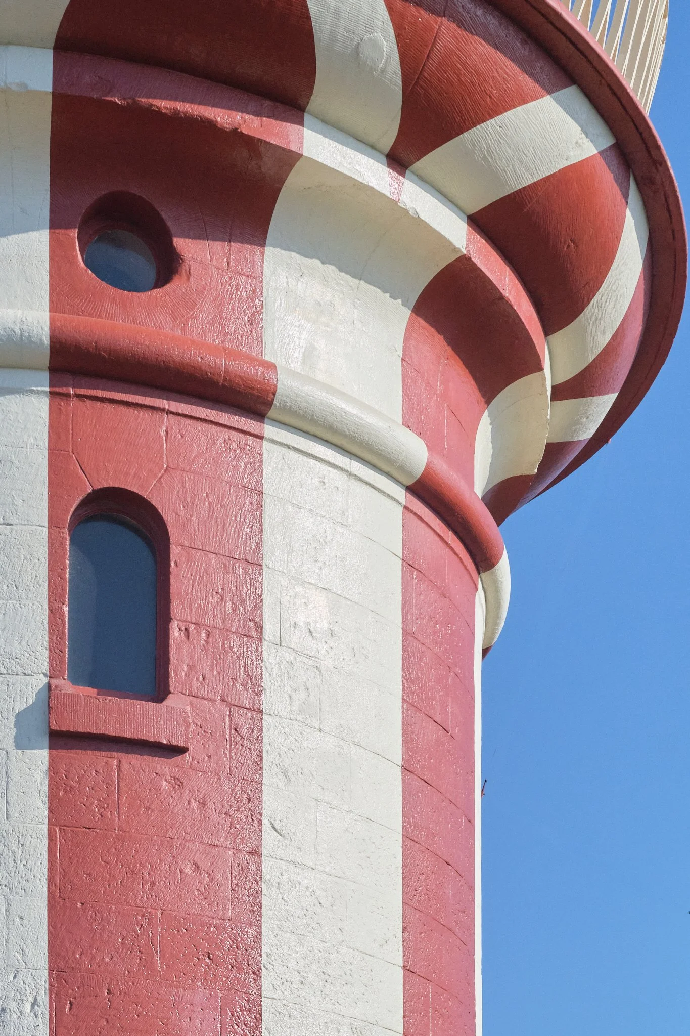 Close-up of a lighthouse with red and white vertical stripes against a clear blue sky.