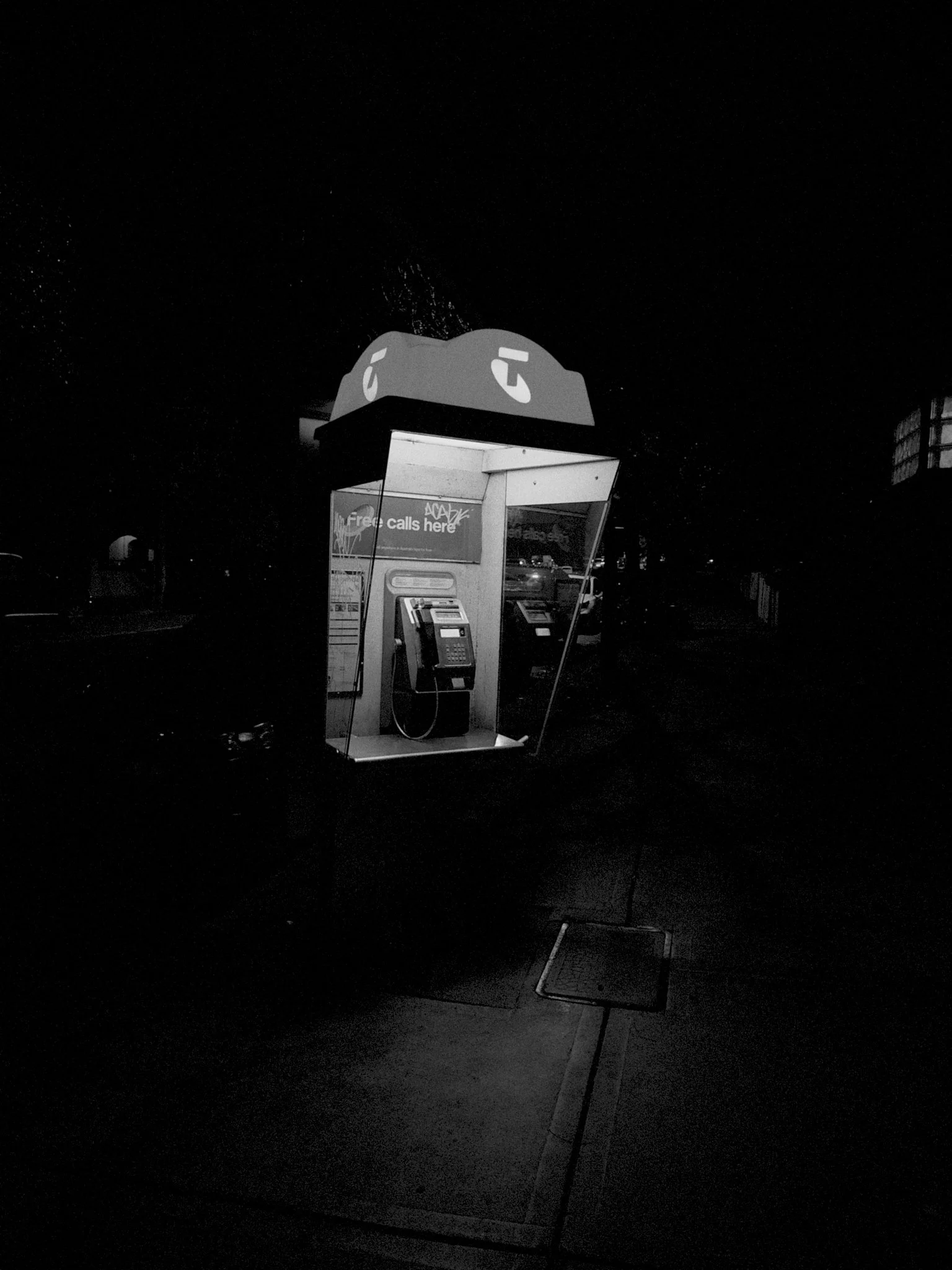 A public payphone booth on a dark street, with a phone and a sign that says 'Free calls here'.