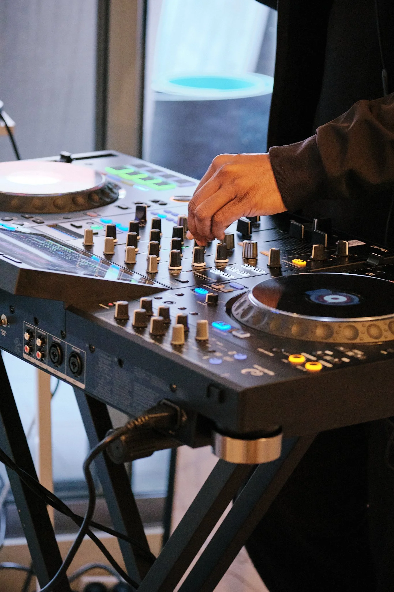 A DJ mixing music on a professional DJ controller with his right hand adjusting knobs.