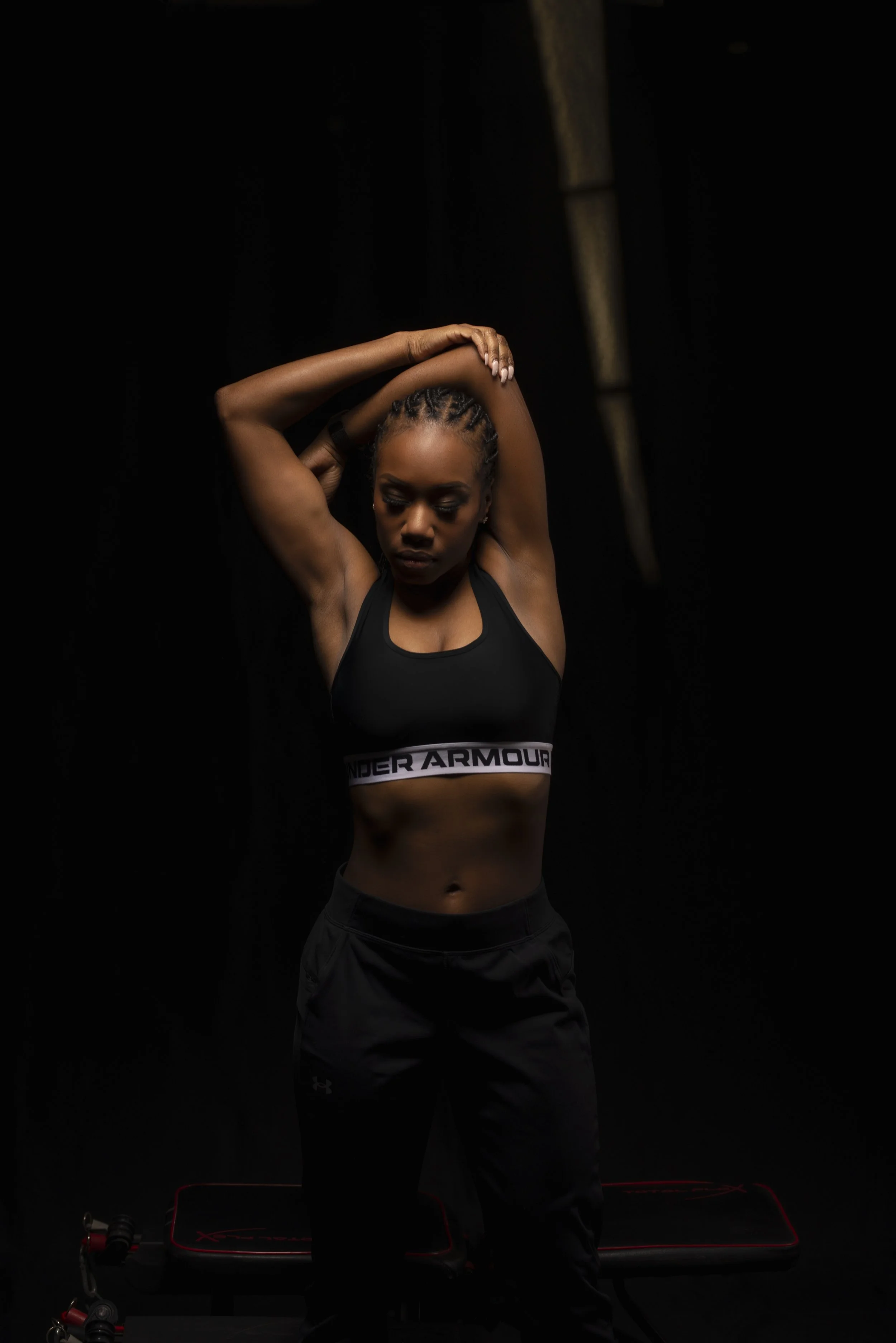 Vanessa Bosse en tenue de sport noire, s'étirant dans un environnement sombre, avec un tapis d'entraînement au sol.