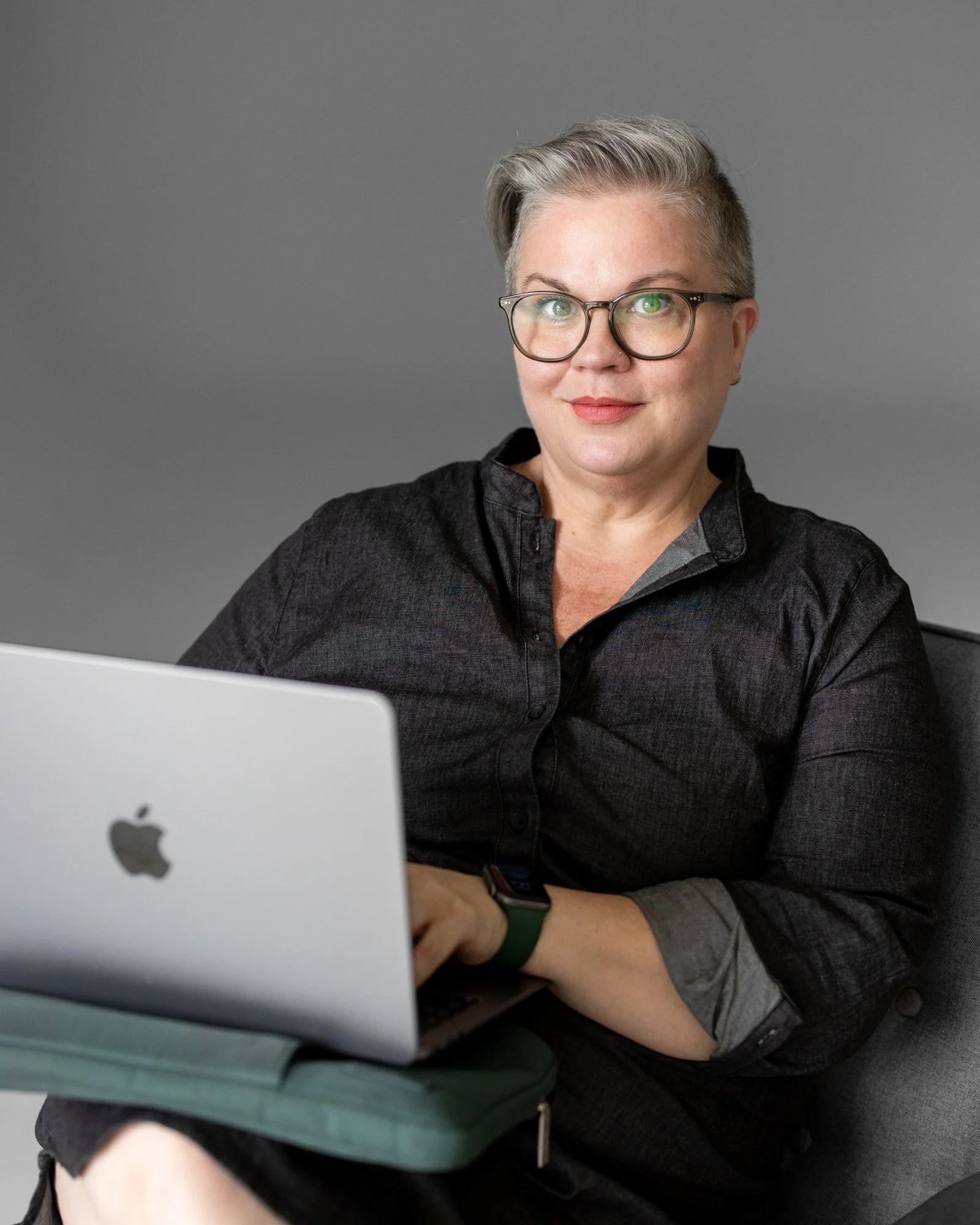 Sarah Braver, COO of coLeague, sits with her laptop as she smiles slightly at the camera.