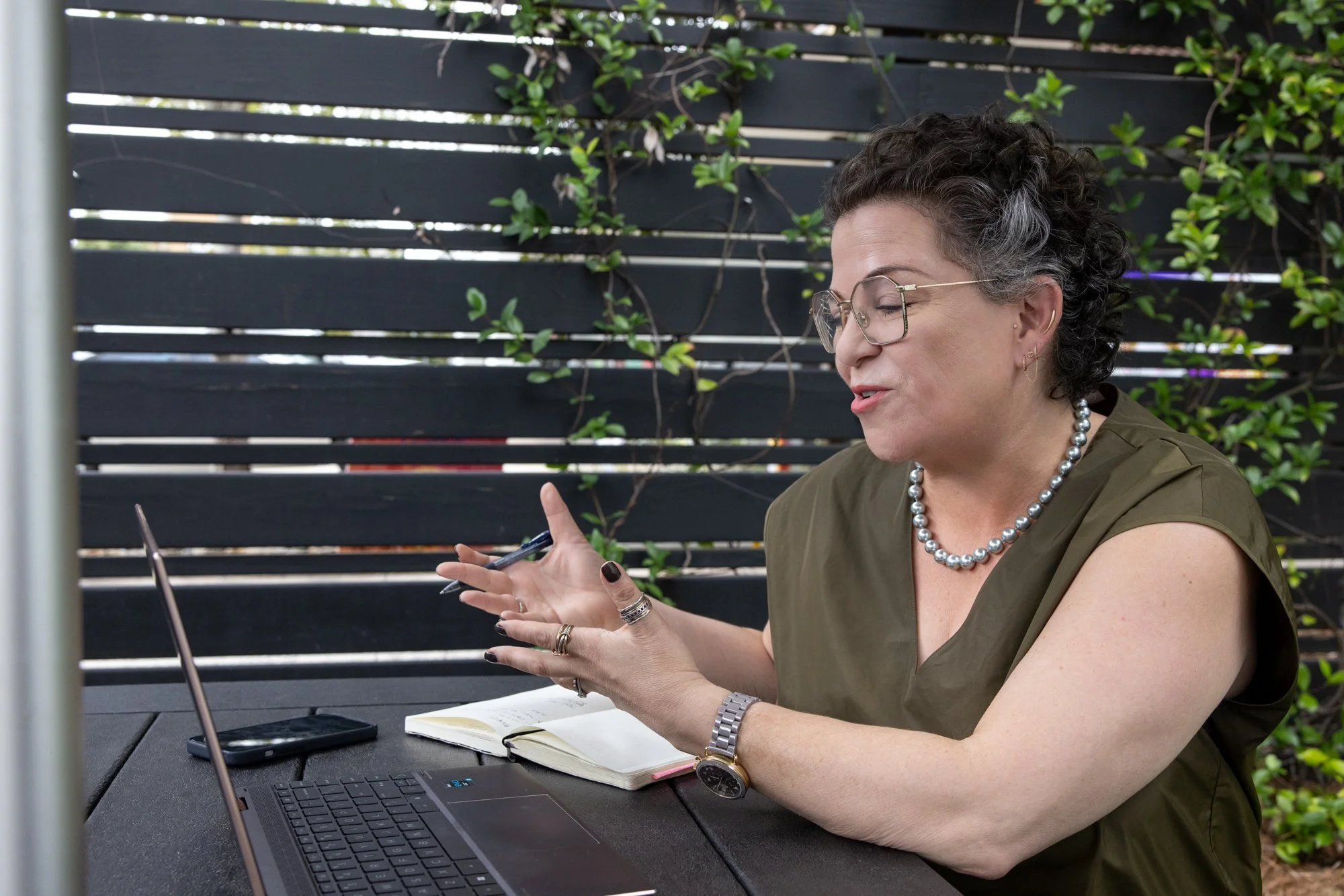 Lora Cover, CEO of coLeague, sits at a picnic table and is talking to a client on a video call on her laptop.