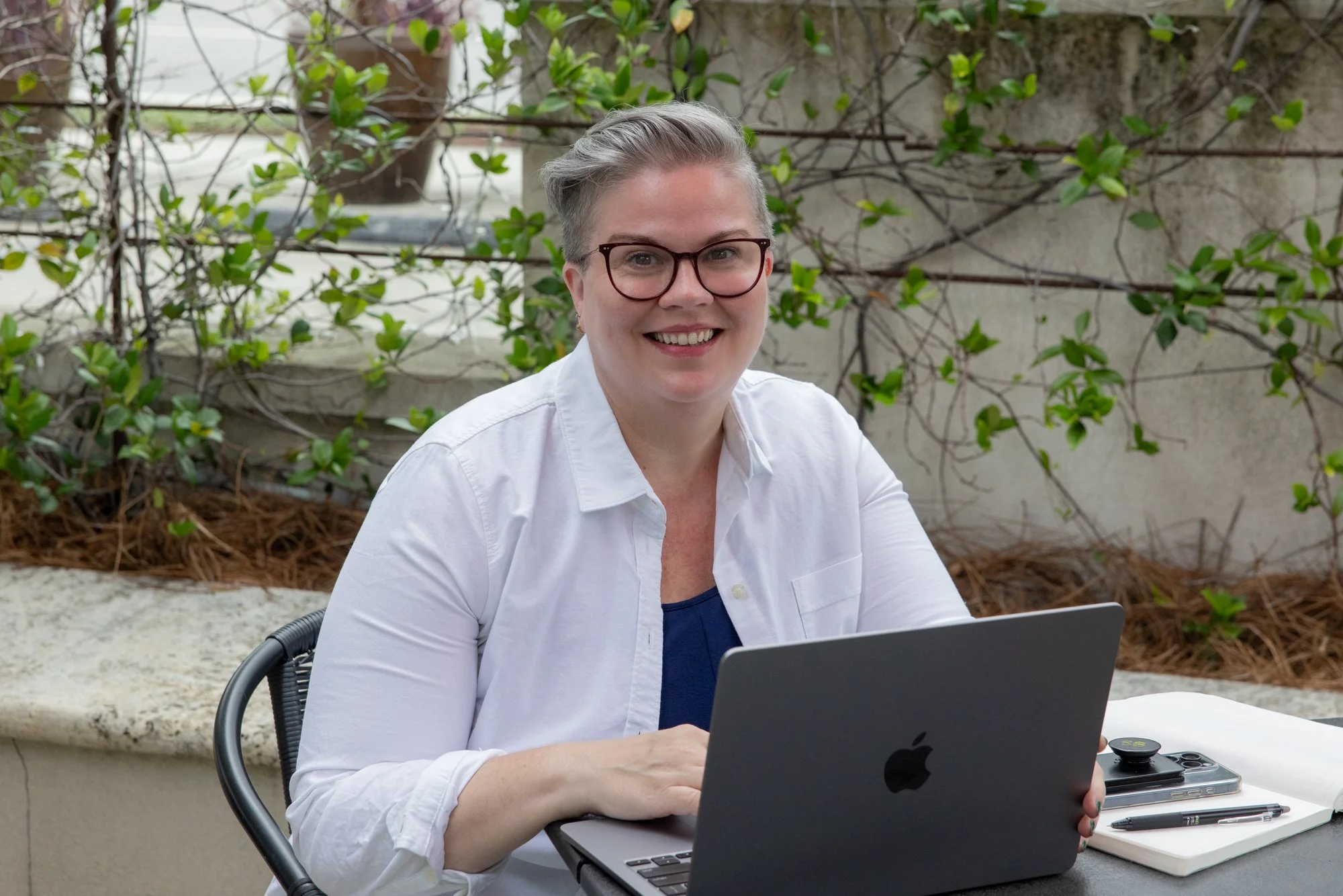 Sarah Braver, COO of coLeague, sits outdoors with her laptop as she smiles widely at the camera.