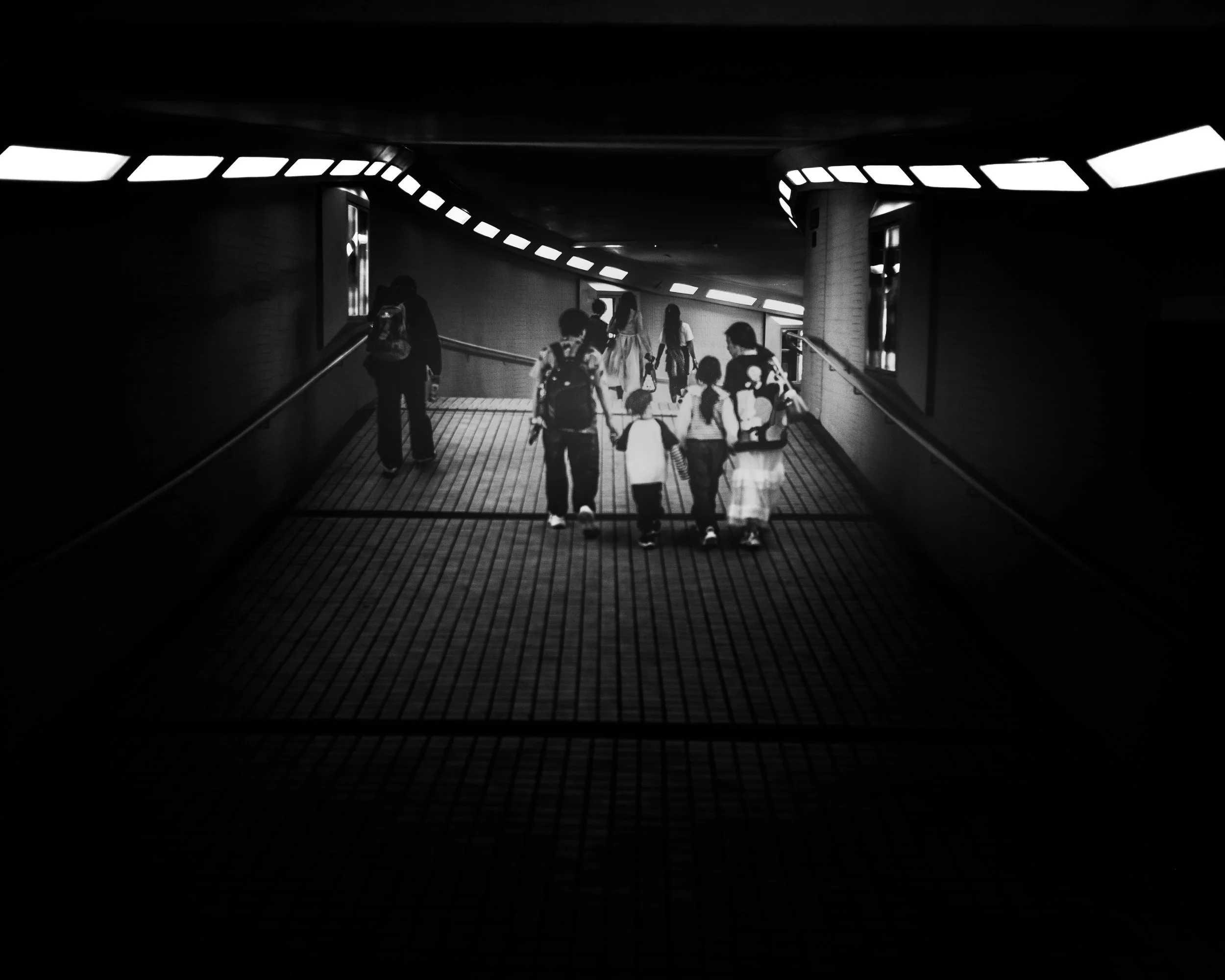 Black and white photo of people walking through a tunnel, some holding hands and carrying backpacks.