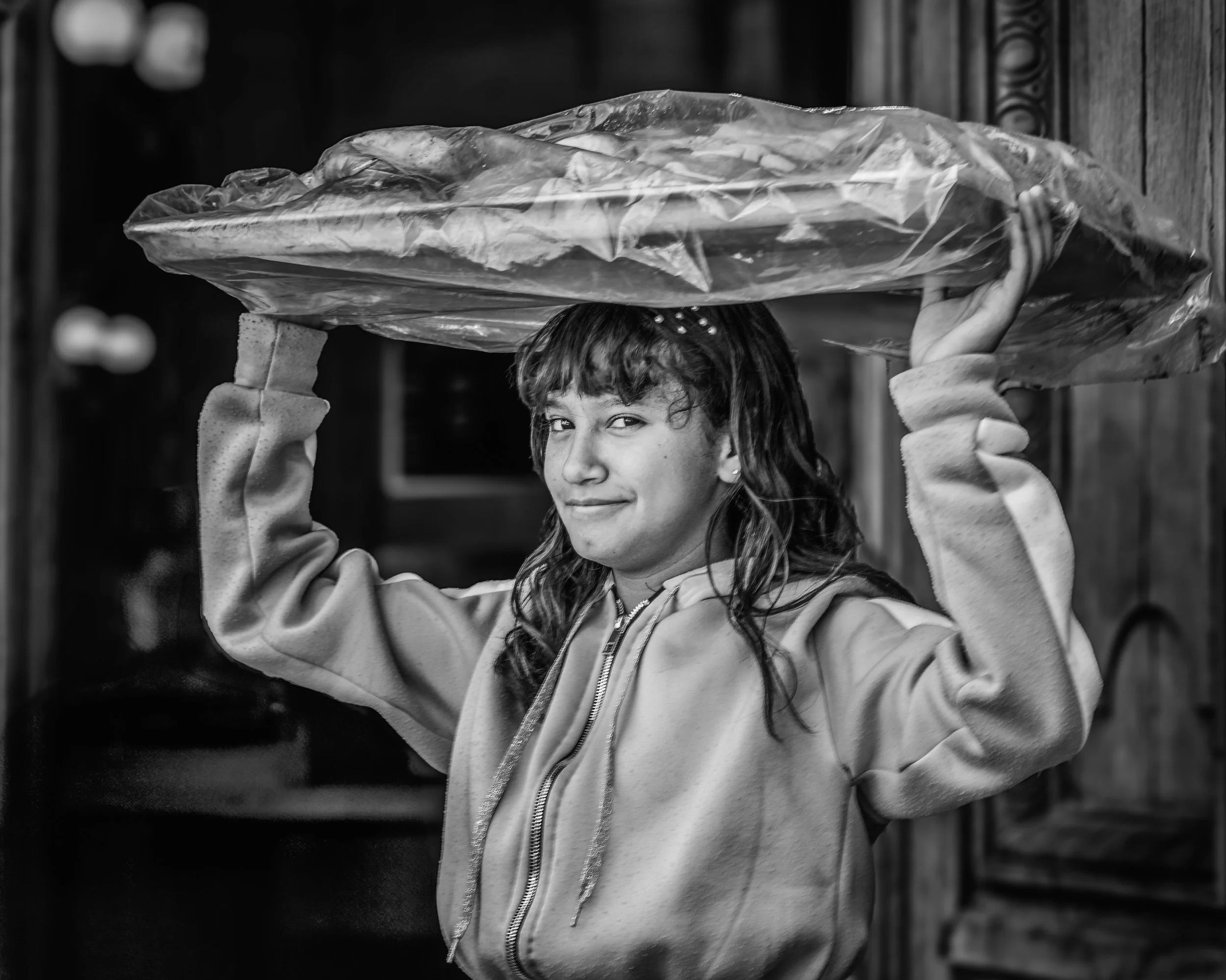A girl with long hair, wearing a jacket, holding a large bag on her shoulder, looking at the camera and smiling slightly.