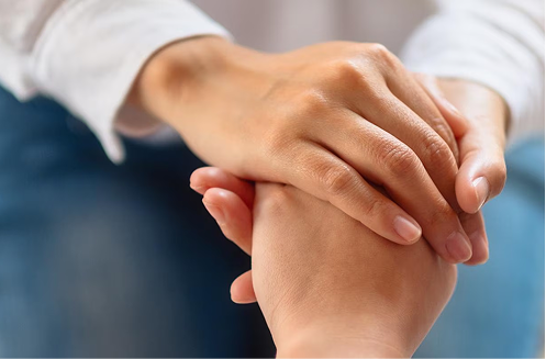 Close-up of one person gently clasping and comforting another person's hand in a supportive gesture.