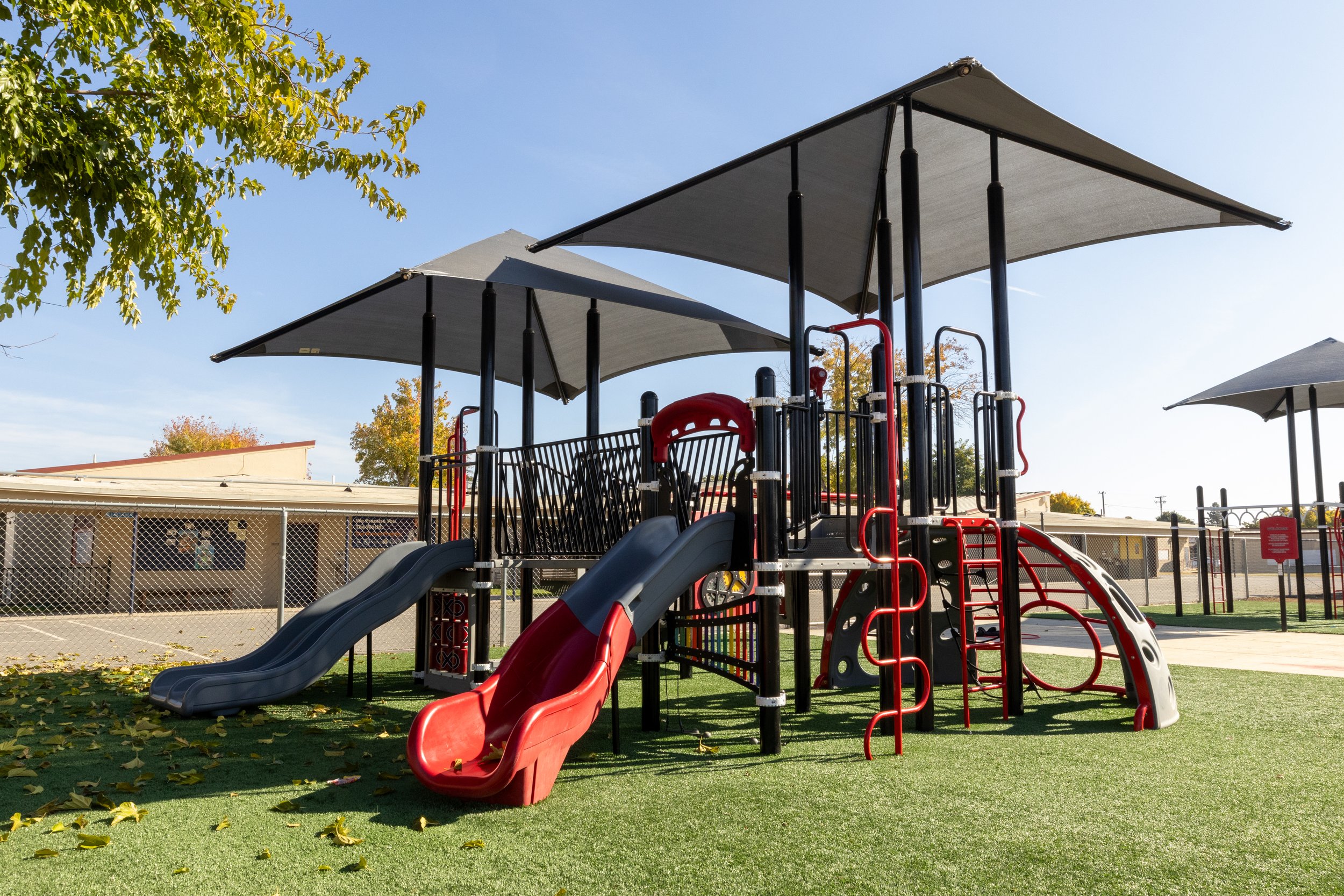 Playground with slides, climbing structures, and sunshades on artificial grass.