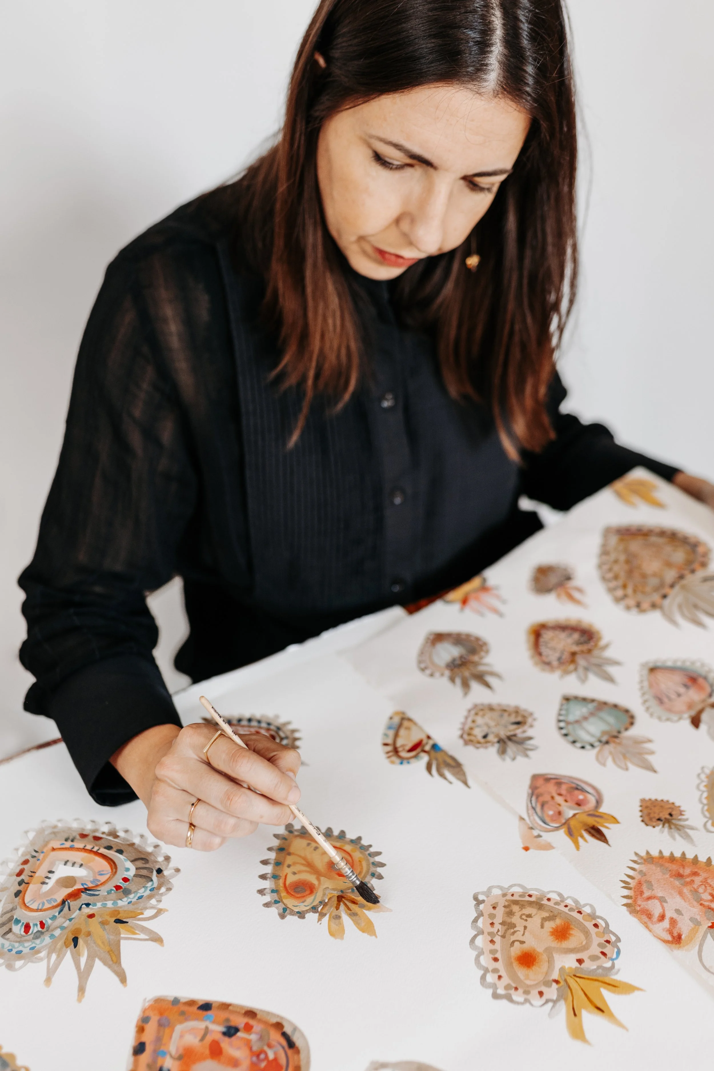 Mujer con cabello castaño y camisa negra decorando hojas de papel con acuarelas y pintura