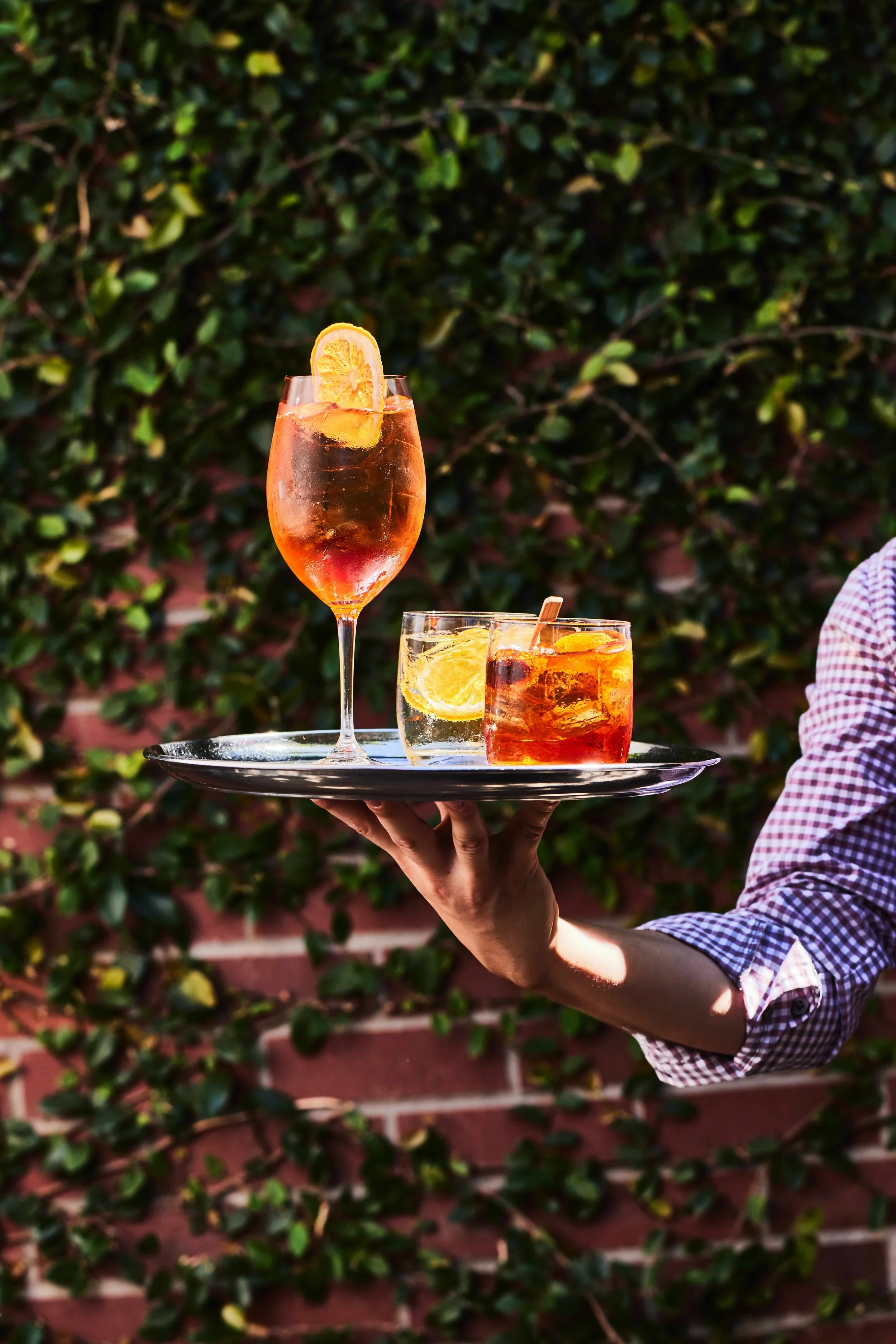 tray of cocktails in front of a brick wall filled with green vines