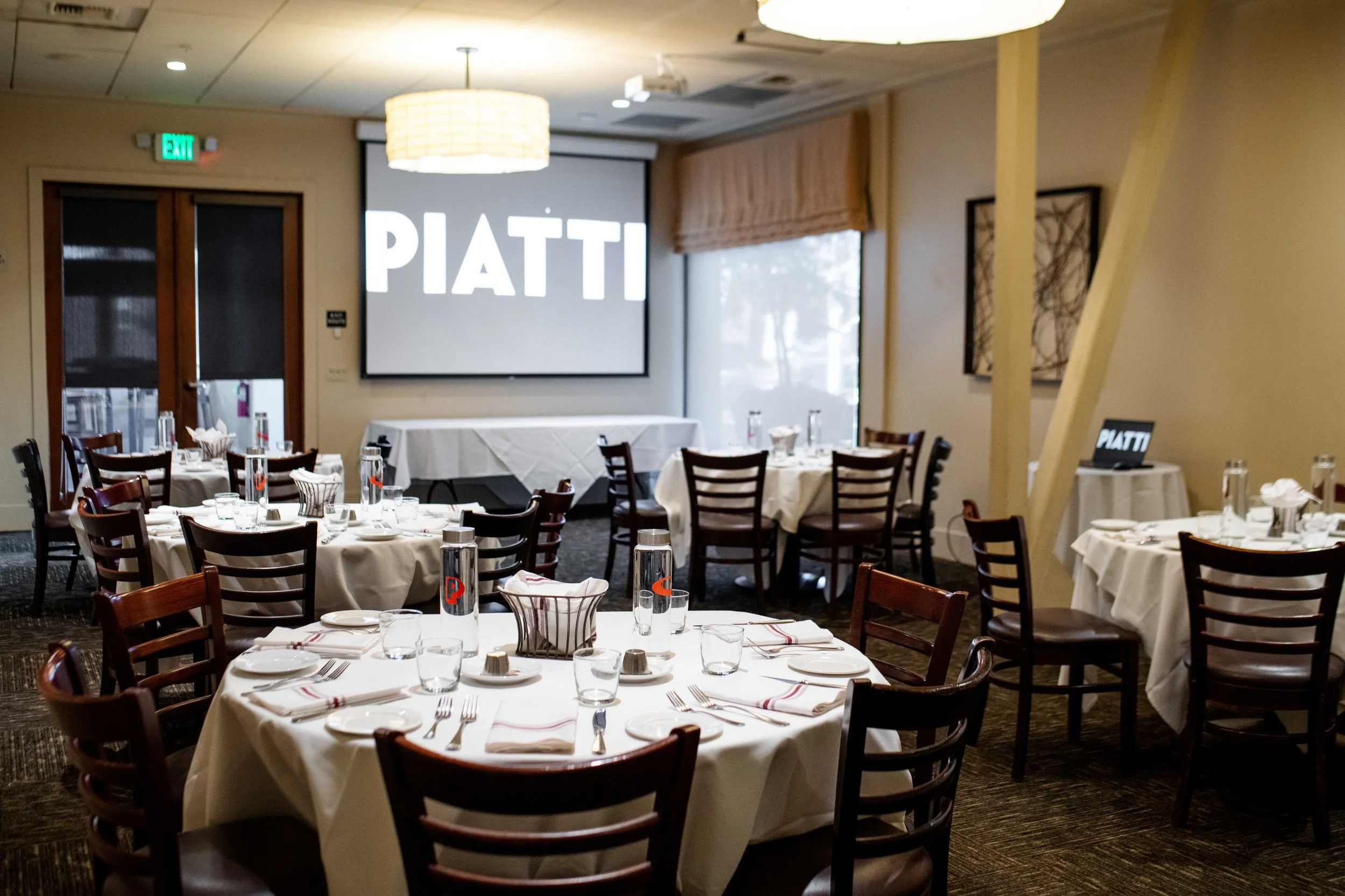 front tuscan room with round tables set up and a projection screen on the wall