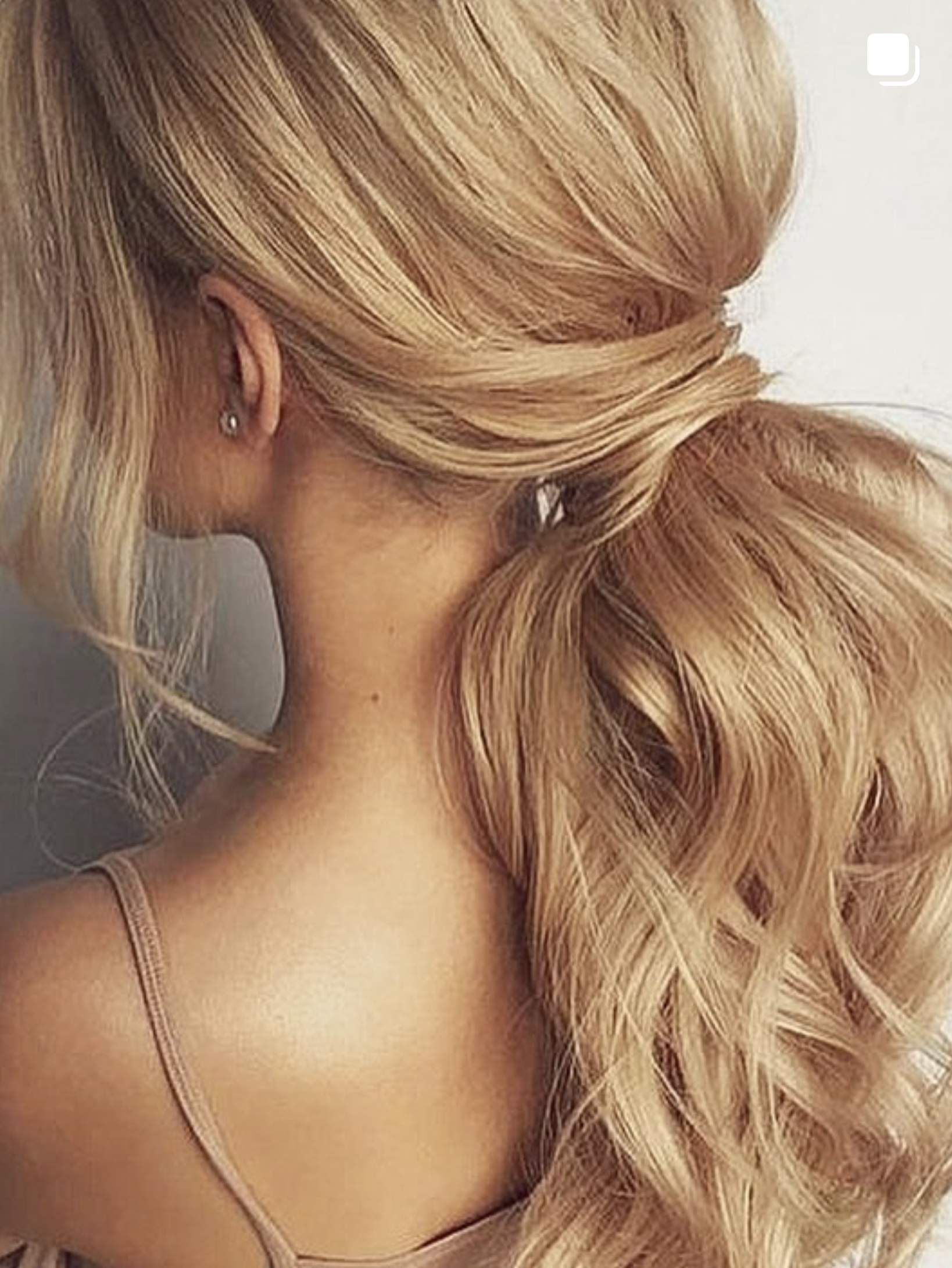 Soft blonde extensions styled into a low ponytail.
