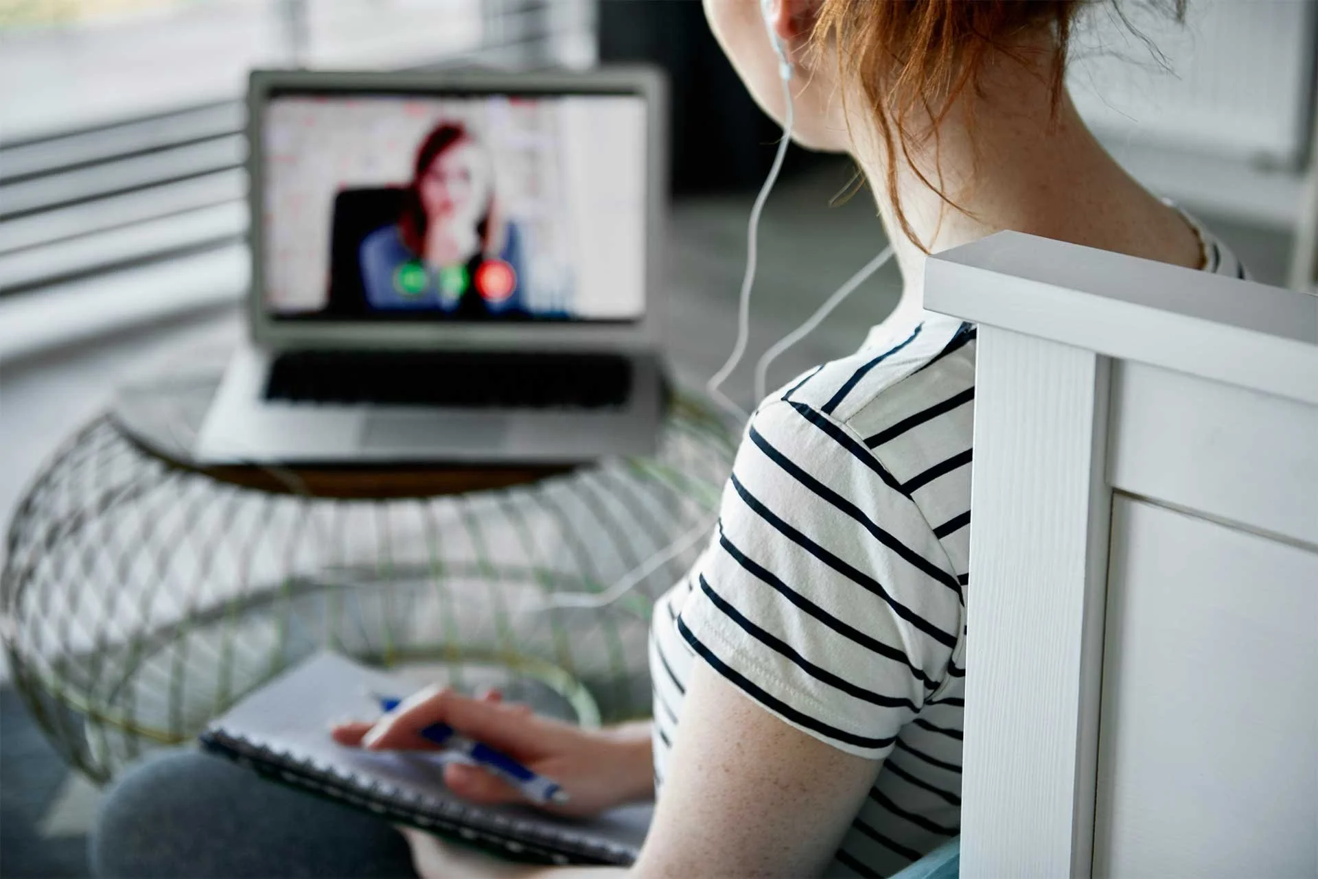Woman wearing earbuds participating in a video call from home on her laptop.