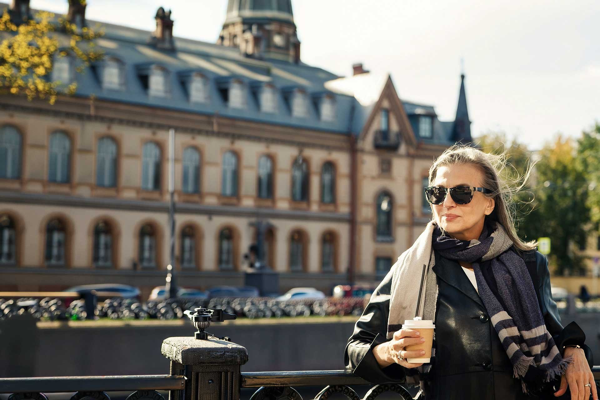 Confident woman holding a coffee outdoors, by herself, looking forwards and smiling softly.