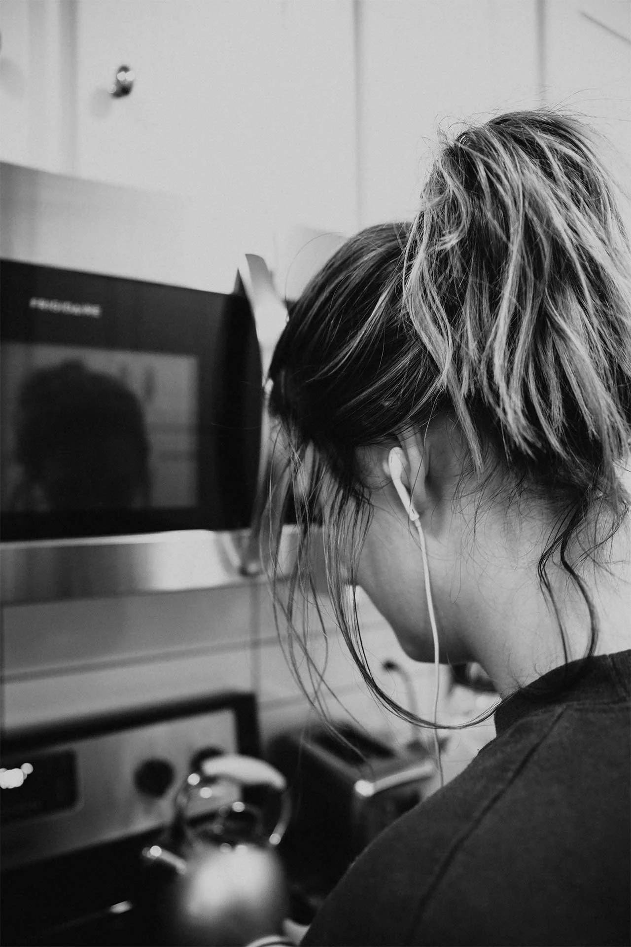 Woman wearing earbuds while preparing food in a kitchen, listening to a podcast as she goes about her day.