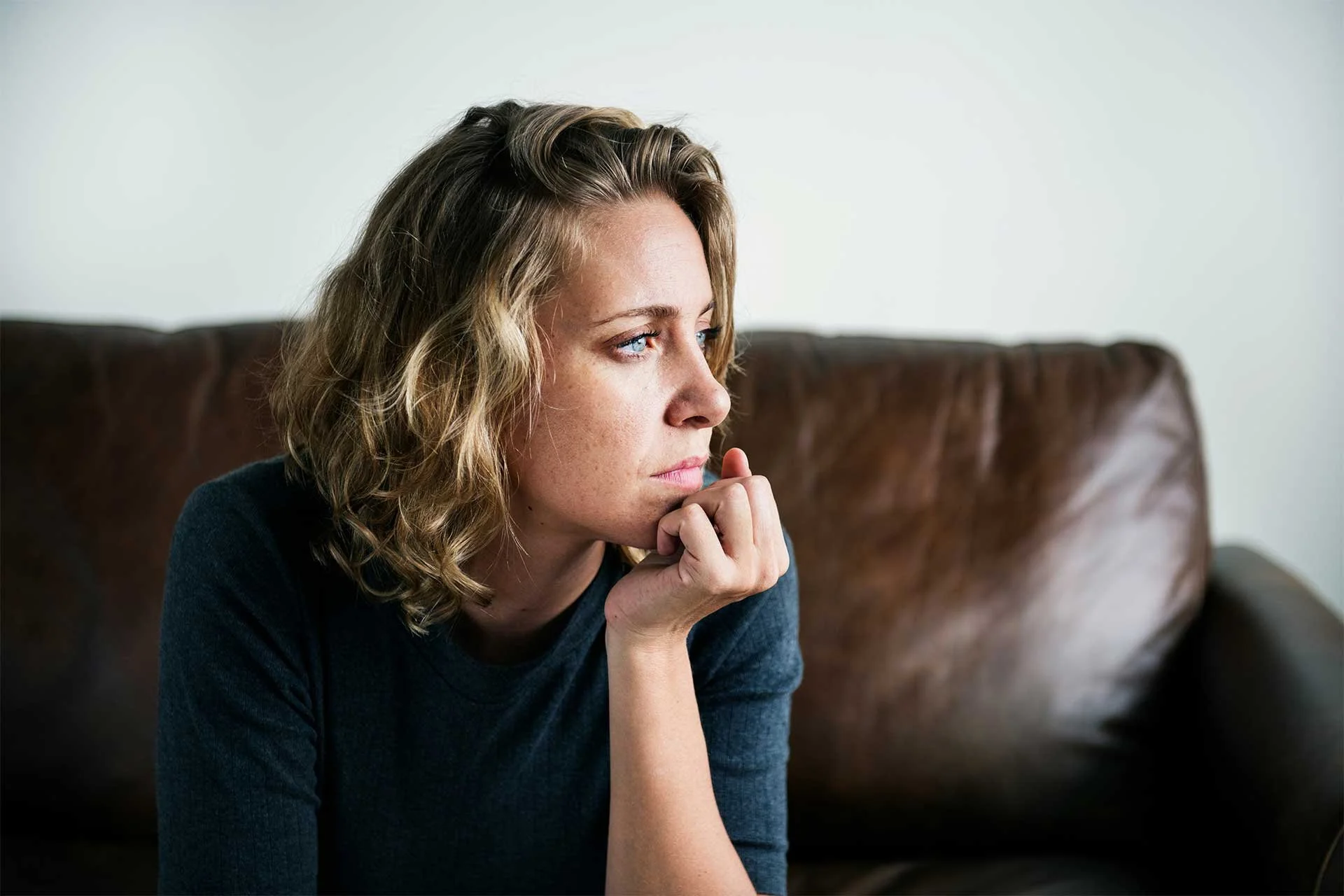 Thoughtful woman sitting alone on a couch, looking into the distance as she considers her next steps.