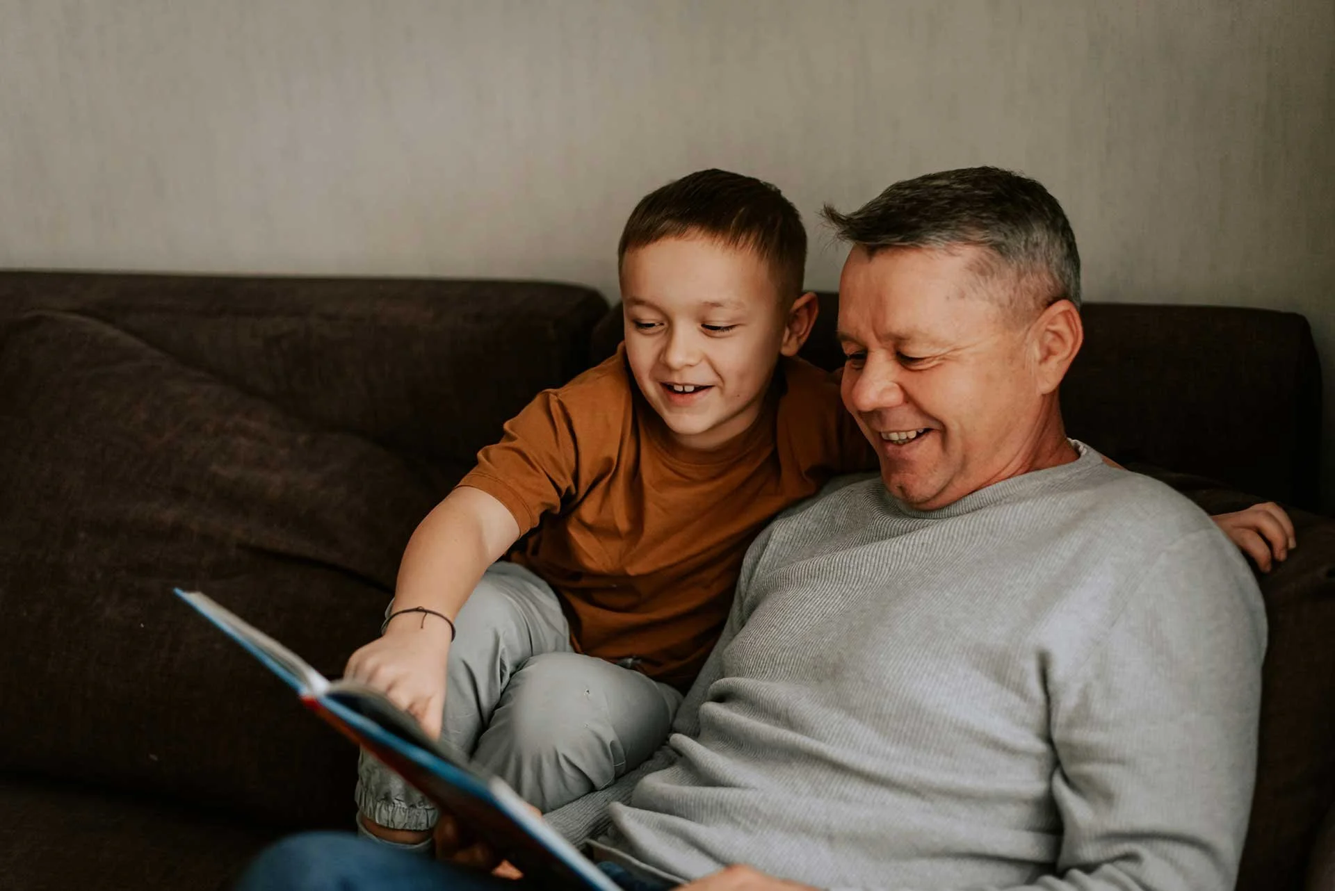 Father and young son smiling together while looking at a tablet on the couch.