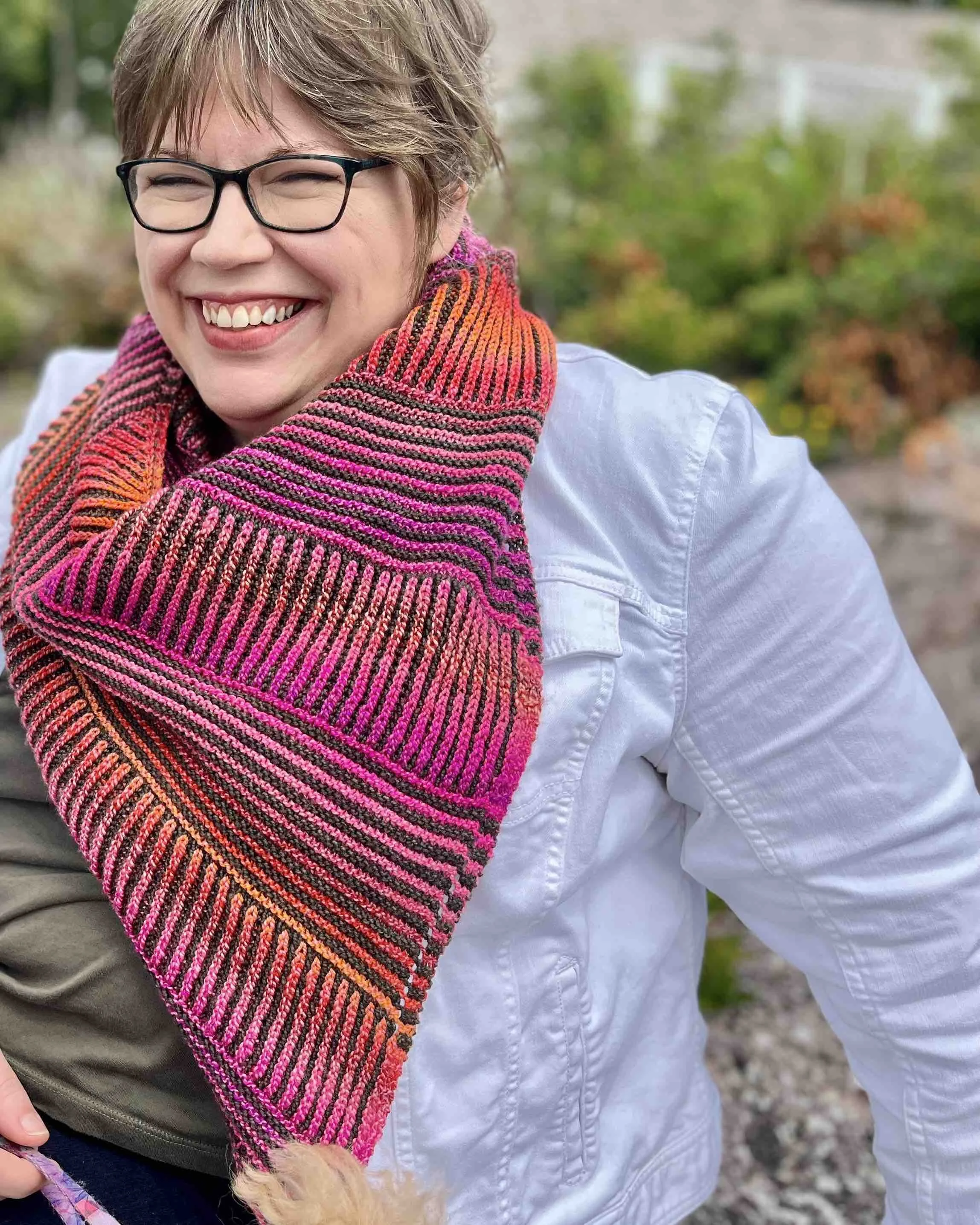 Katie, a white woman with light brown hair, wears a bright pink and orange Montrose cowl over a white jean jacket