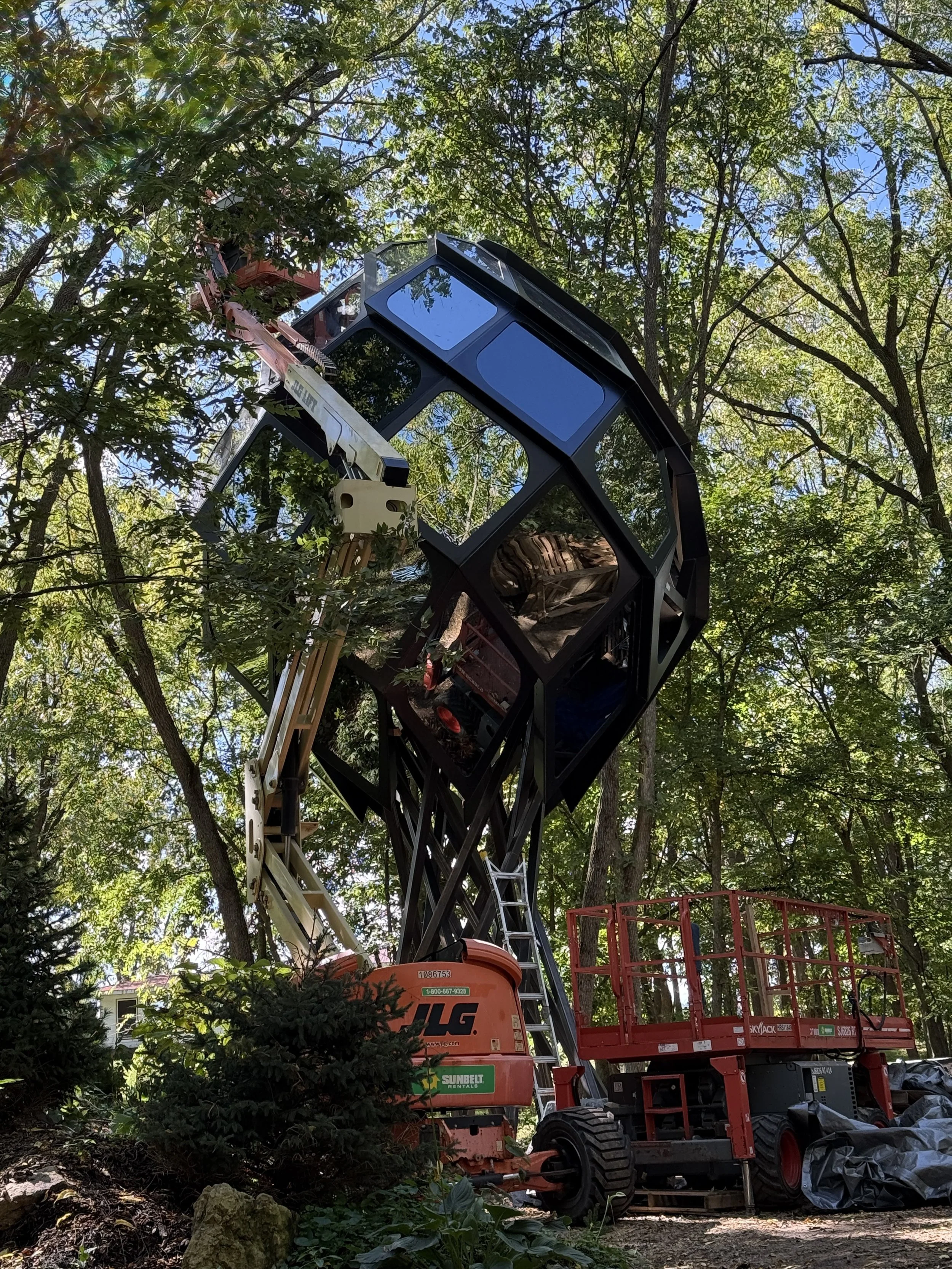 construction equipment next to a glass treehouse set in a forest.