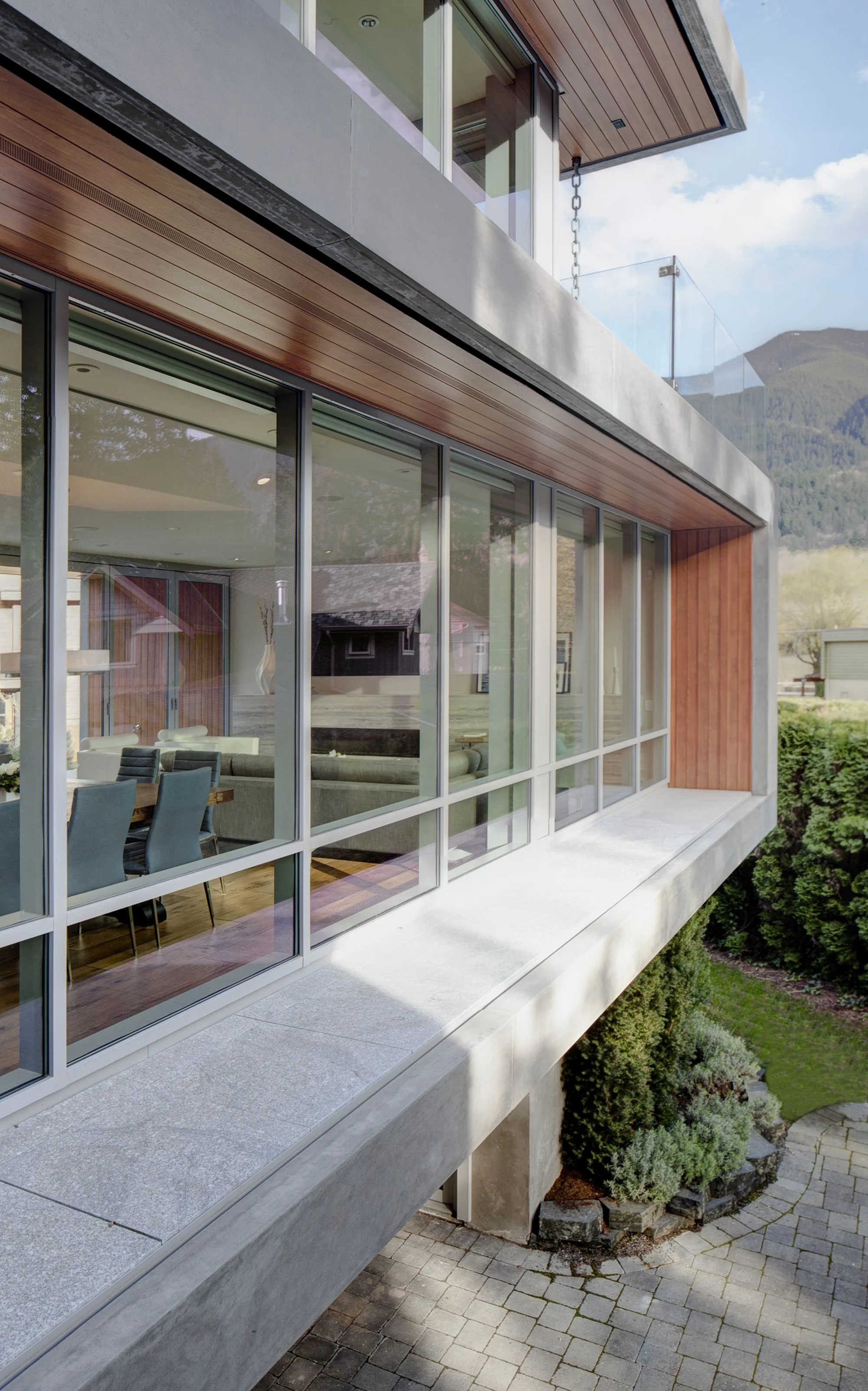 Modern house with large glass windows, wooden accents, concrete elements, and a landscaped yard.