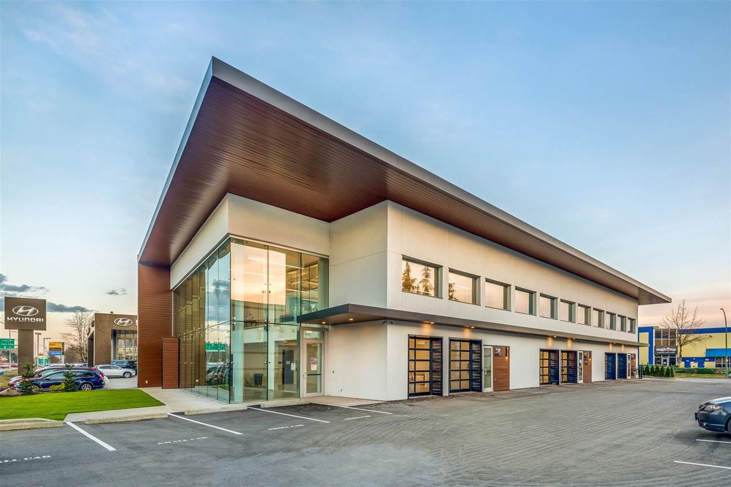 Modern commercial building with glass entrance and parking lot, Hyundai dealership visible in background, during daytime.