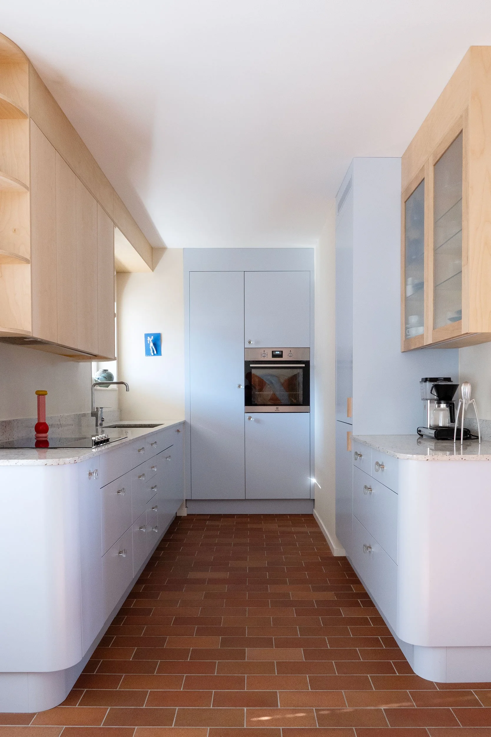 The Pomo Kitchen in Stockholm by Studio Navet — pastel blue cabinetry, natural wood, granite counter, and terracotta tiles in a postmodern apartment.