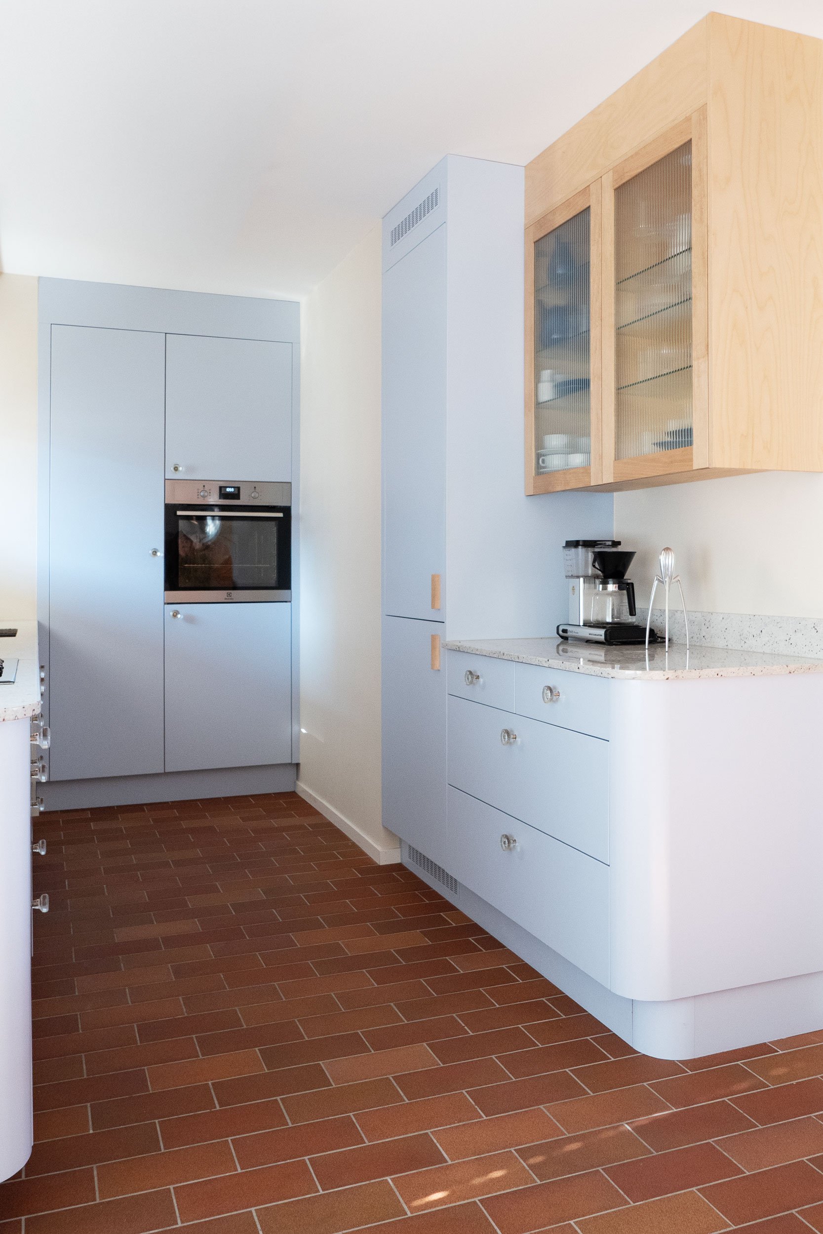 The Pomo Kitchen in Stockholm by Studio Navet — pastel blue cabinetry, natural wood, granite counter, and terracotta tiles in a postmodern apartment.