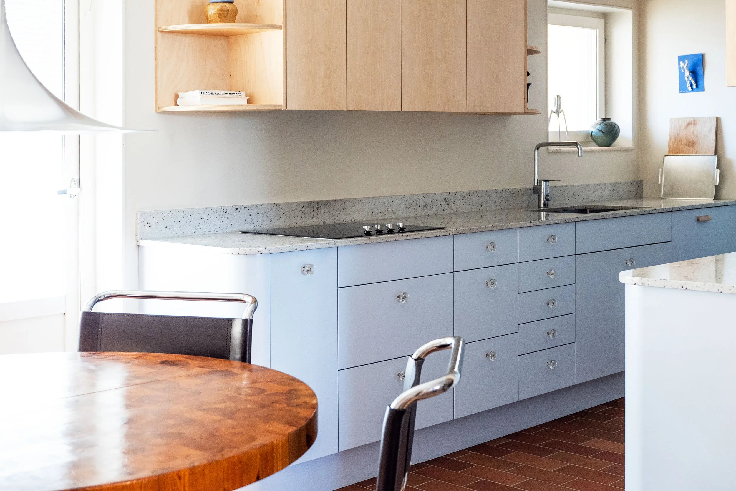 The Pomo Kitchen in Stockholm by Studio Navet — pastel blue cabinetry, natural wood, granite counter, and terracotta tiles in a postmodern apartment.