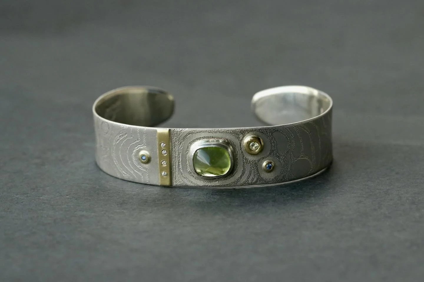 Earthy, modern, distinct caliber of self worth.
.
PERIDOT BRACELET/ 18K GOLD/ WHITE DIAMONDS/ SAPPHIRES/ STIPPLE TEXTURED SILVER
.
.
#peridotjewelry 
#greenaesthetic 
#studiojewelry 
#cuffbracelet 
#jewelryart 
#personalstyle 
#uniquejewellery 
#bigs