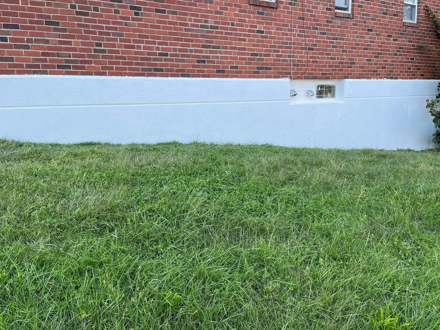 A brick house with a white-painted basement wall painted by Joseph's Coat of Colors LLC in East Falls, PA
