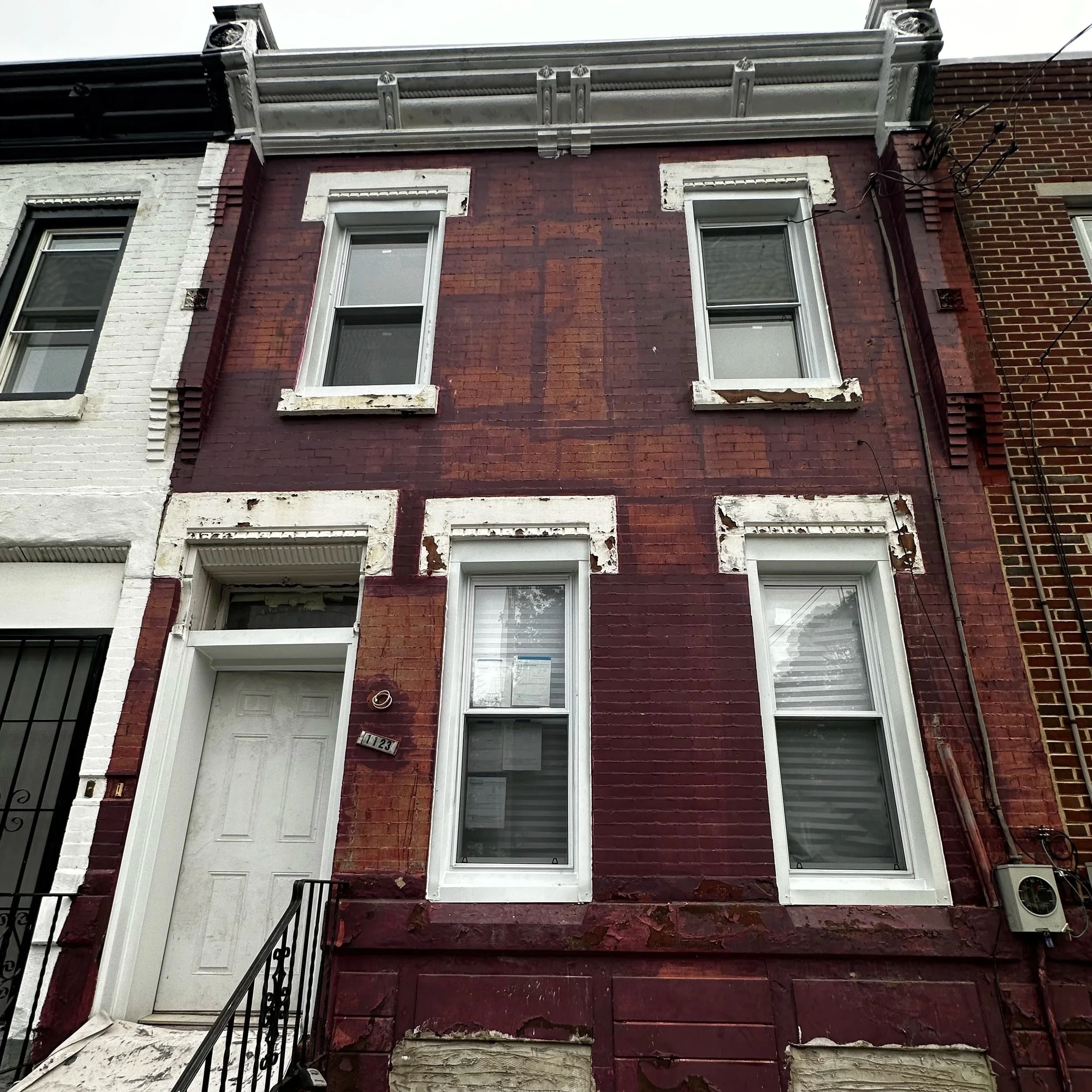 Front view of a three-story brick building with peeling paint and damaged window frames, featuring three white-framed windows on each floor. This is being prepped by Joseph's Coat of Colors LLC