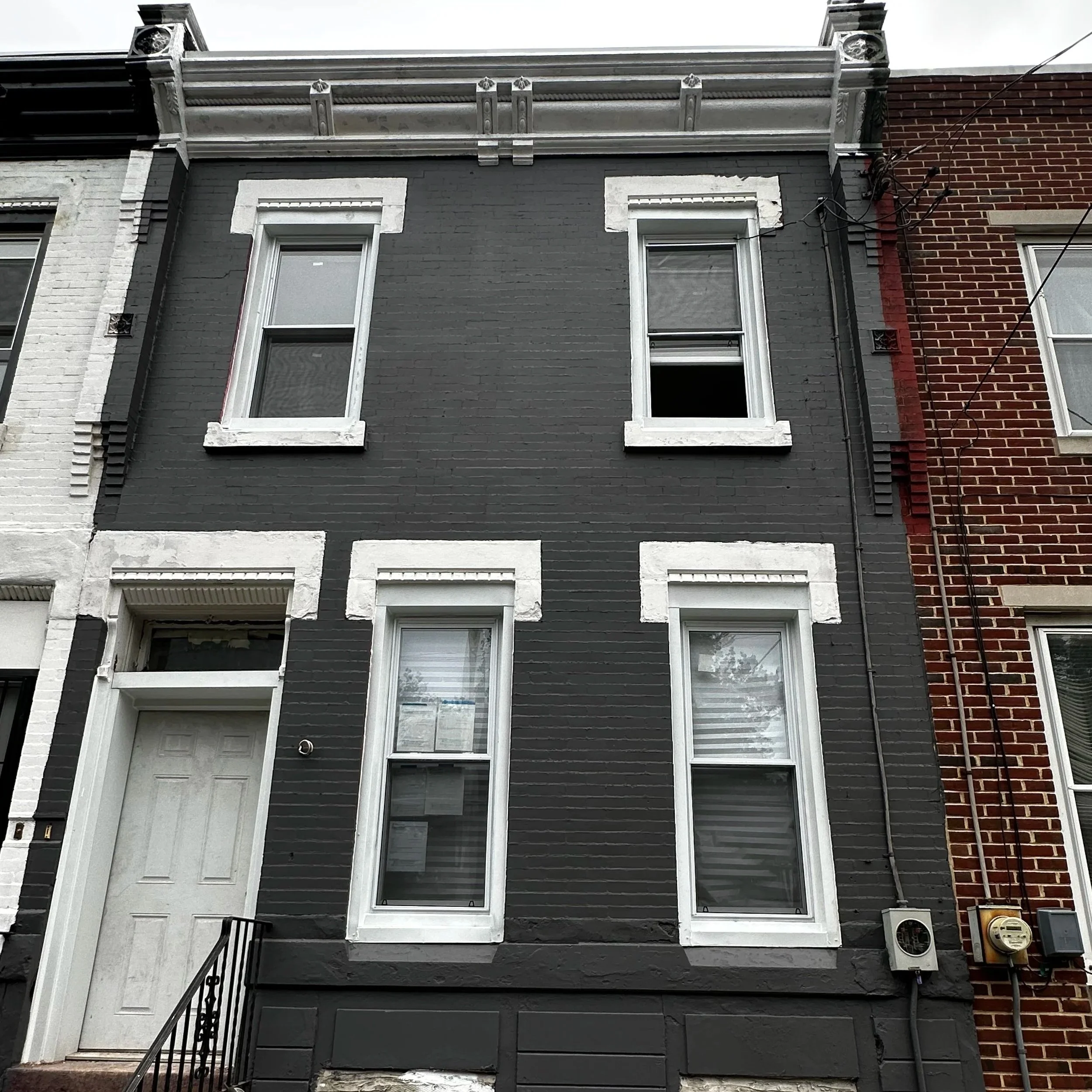A three-story row house painted dark gray with white window sashes and trim, adjacent to a red brick building. Building was painted by Joseph's Coat of Colors LLC