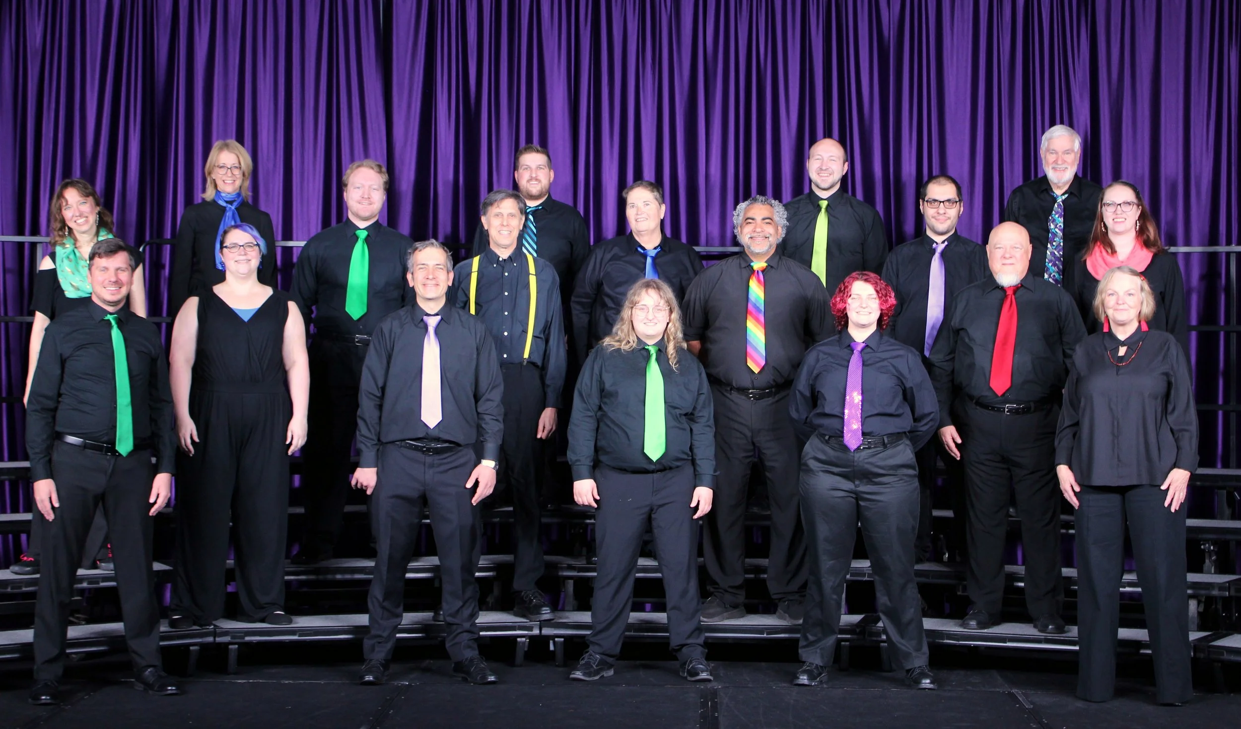 A small chorus in black outfits with color accents against a blue curtain