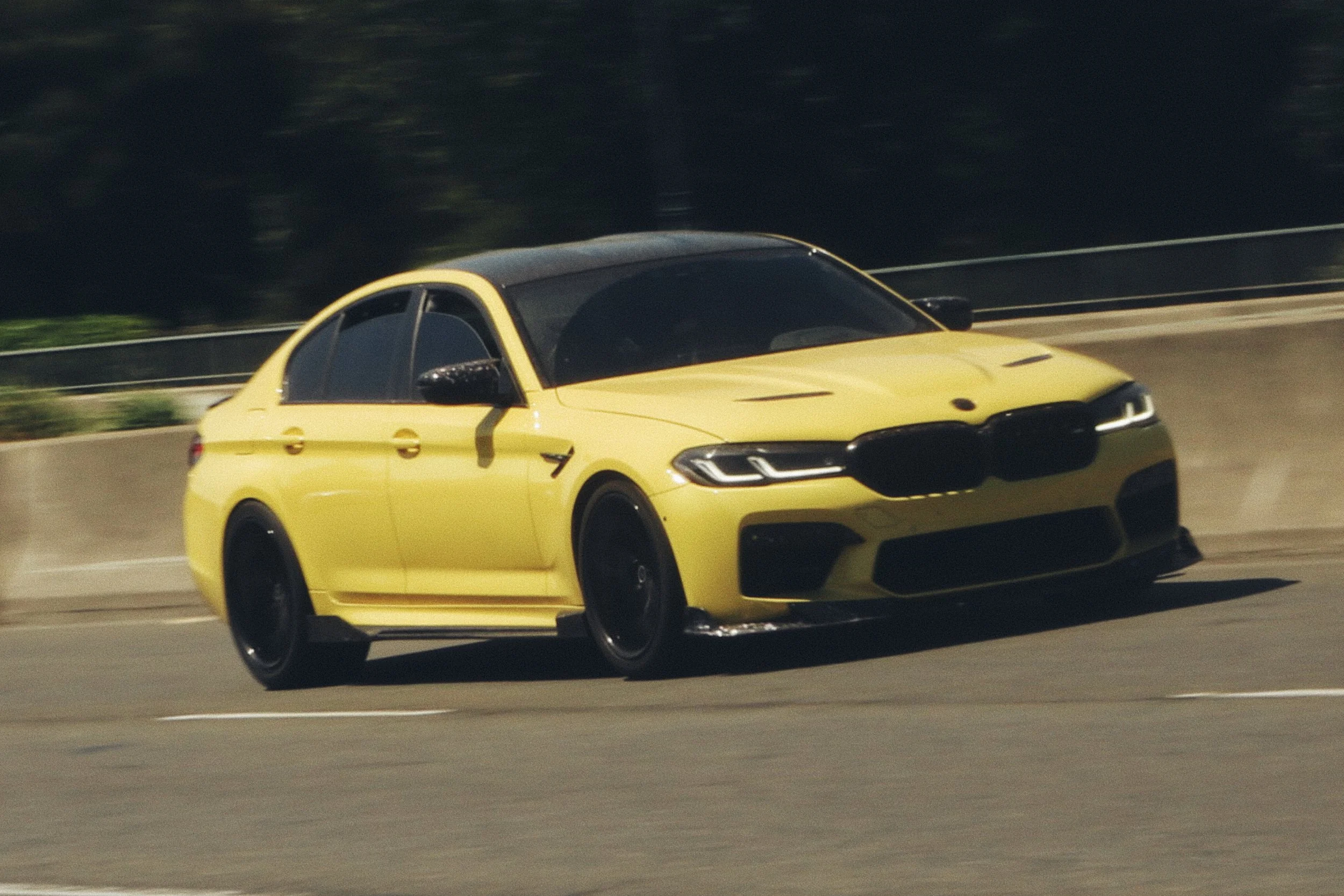 A yellow BMW M5 speeding along a road at night.