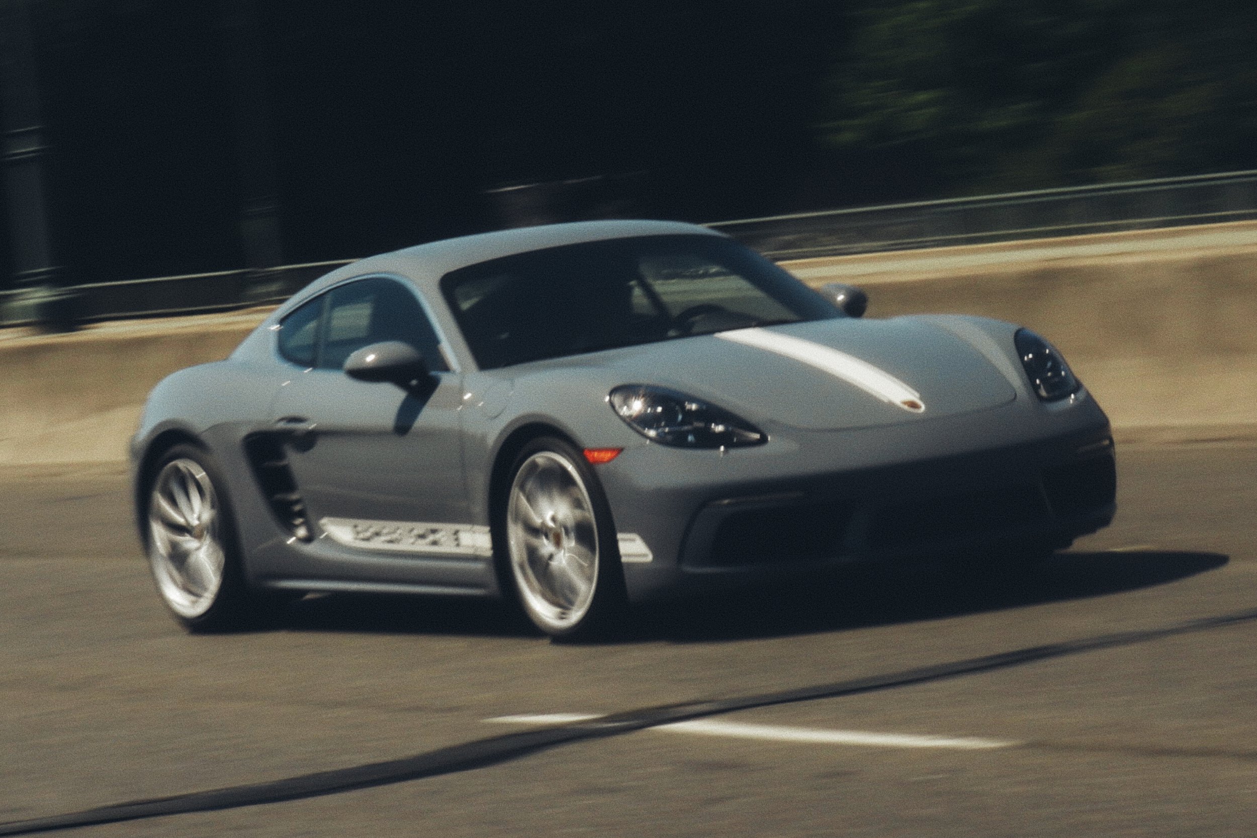 A gray Porsche sports car with white racing stripes on the hood, driving on a race track.