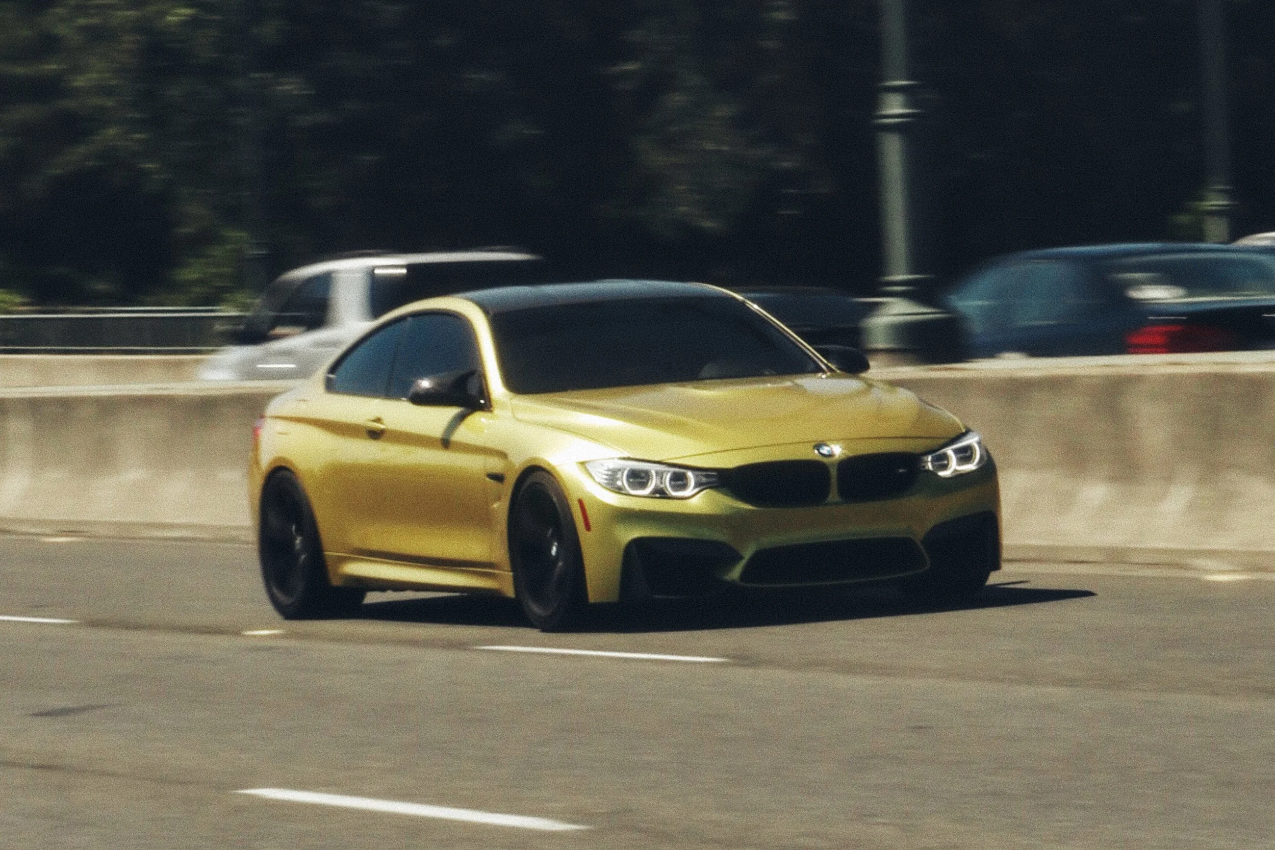 A yellow BMW M4 driving on a busy road with other cars in the background.
