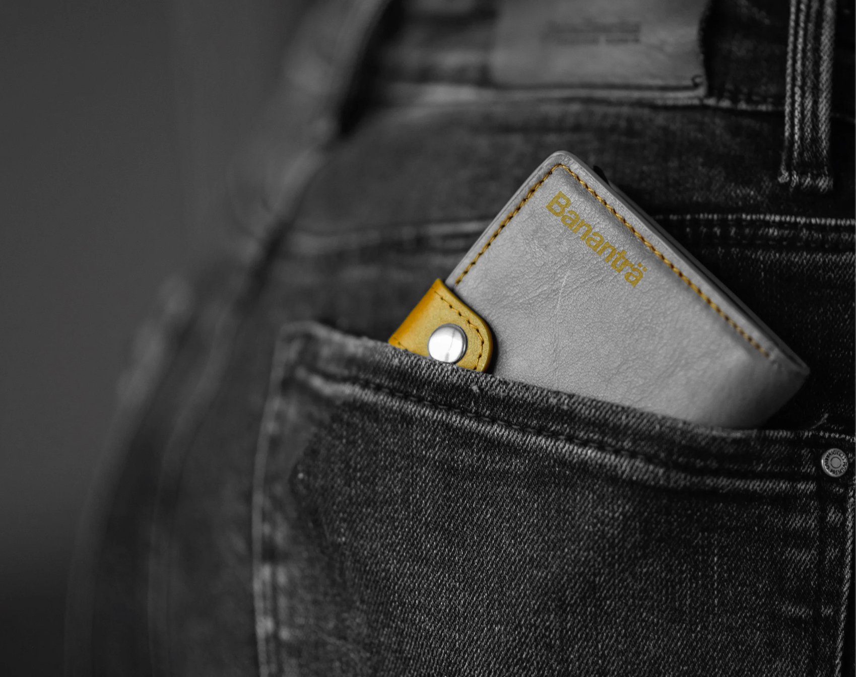 Close-up of a person's black jeans pocket with a gray and yellow Bananträ wallet partially visible inside.