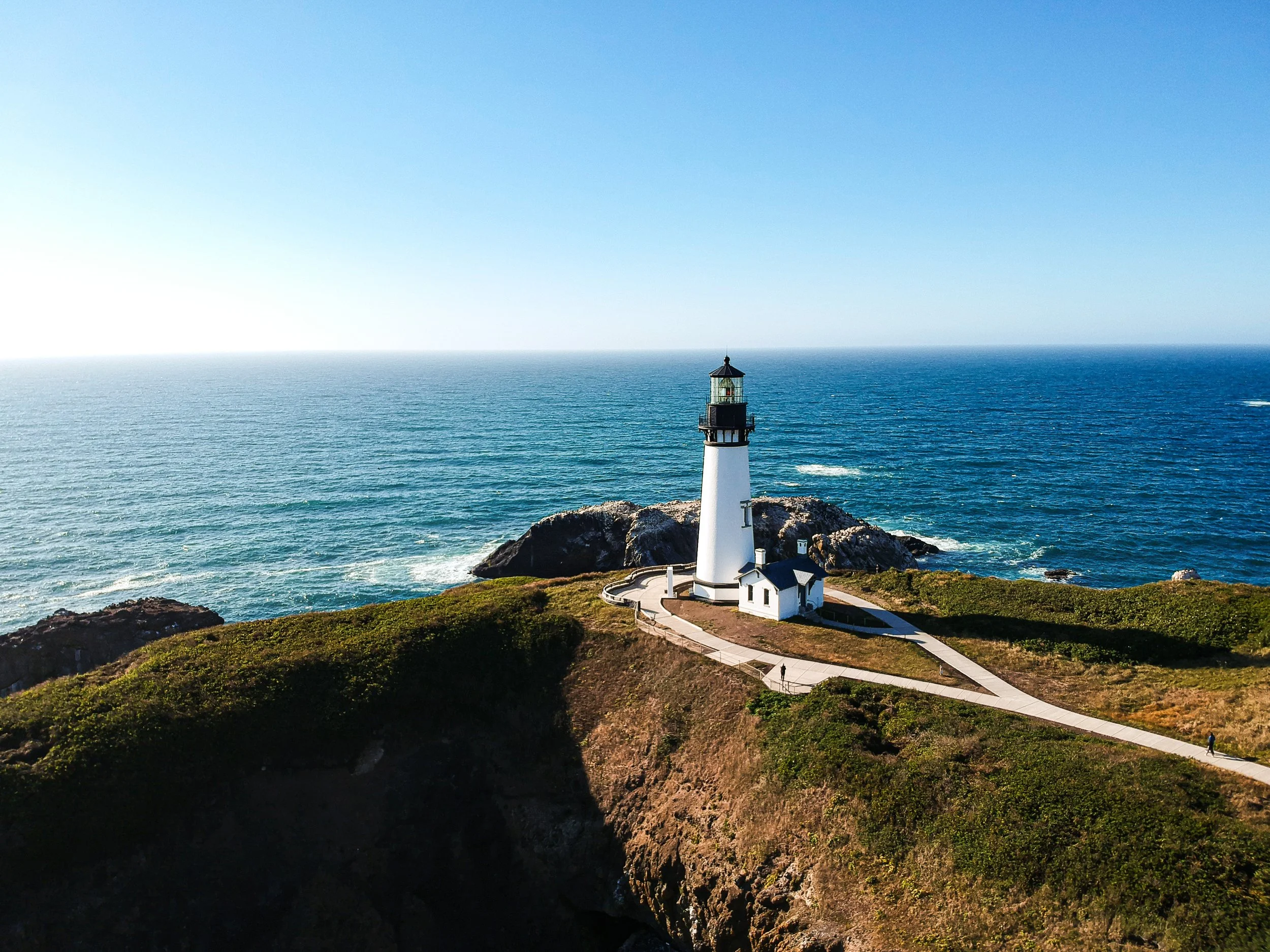 A lighthouse on the rocky Oregon coast near Tillamook with the Pacific ocean in the background under a clear blue sky.