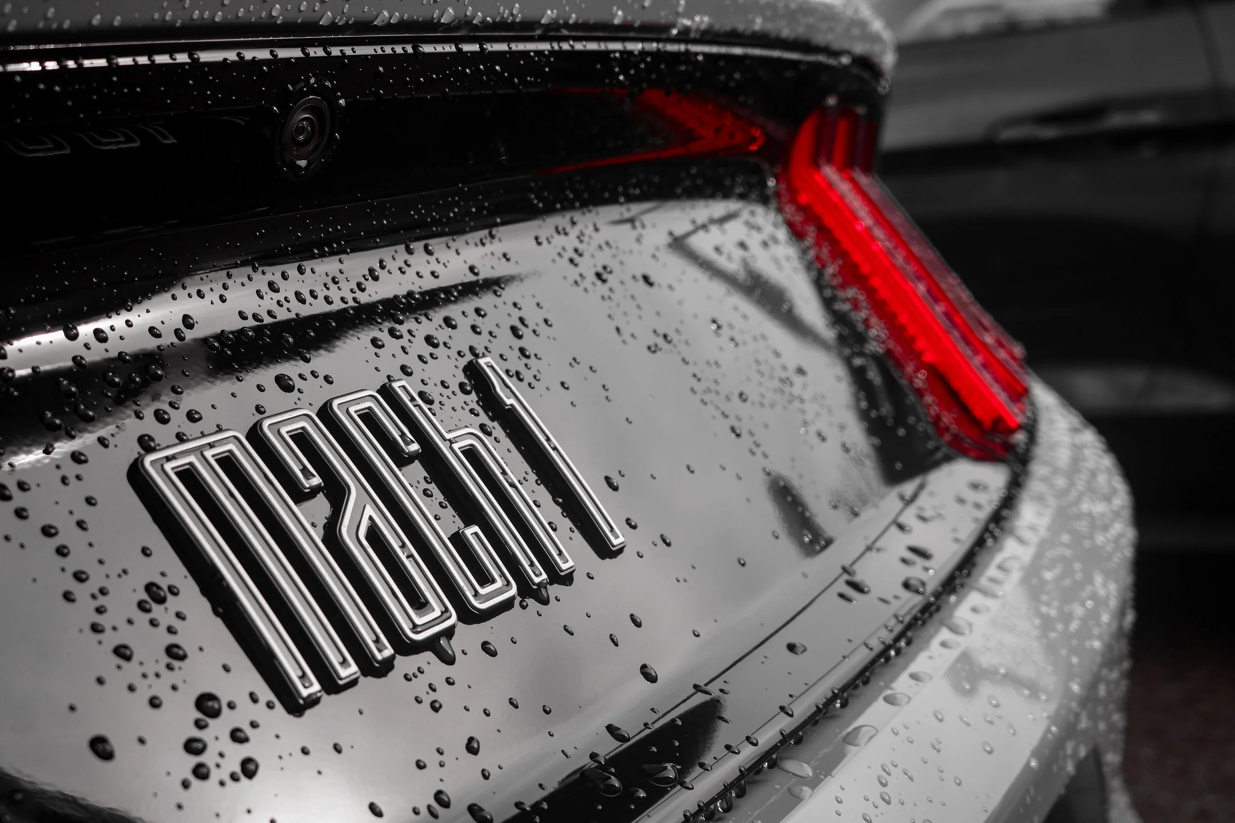 Close-up of a black Audi car's rear, showing the Audi logo and the tail light, with raindrops on the surface.