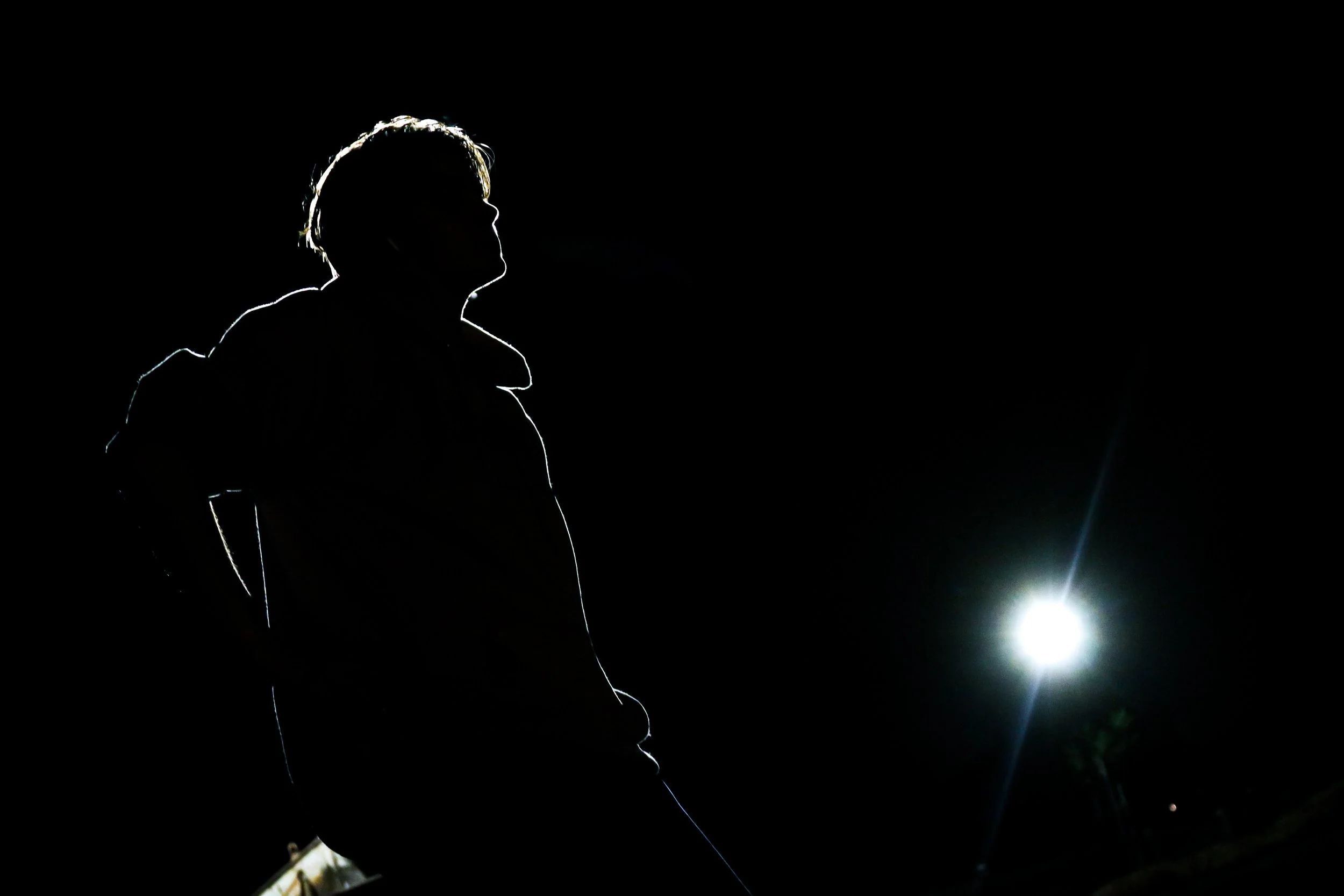 Silhouette of a person standing outdoors at night with a bright light in the background.