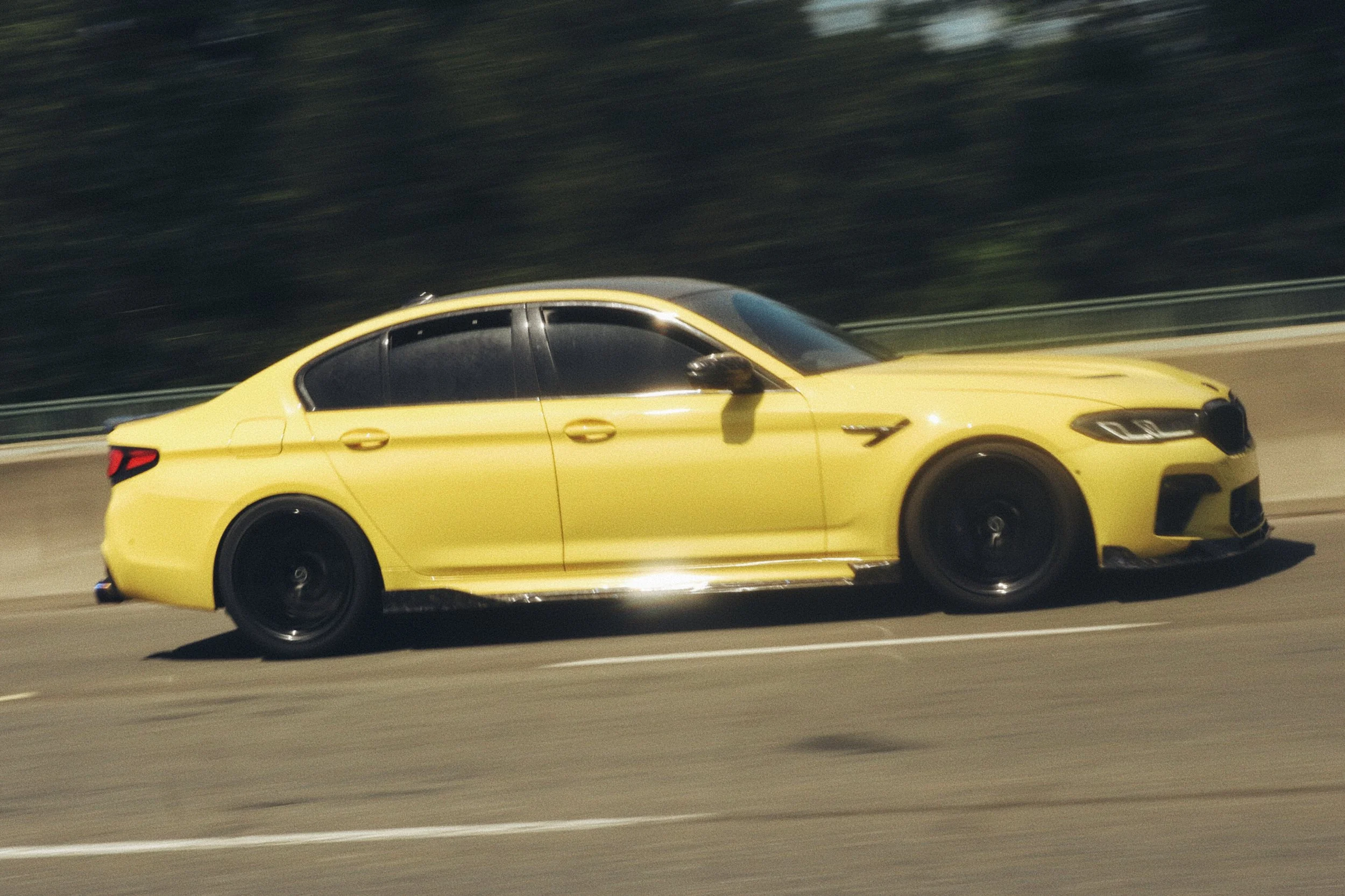 Yellow BMW M5 driving at high speed on a highway during daytime.