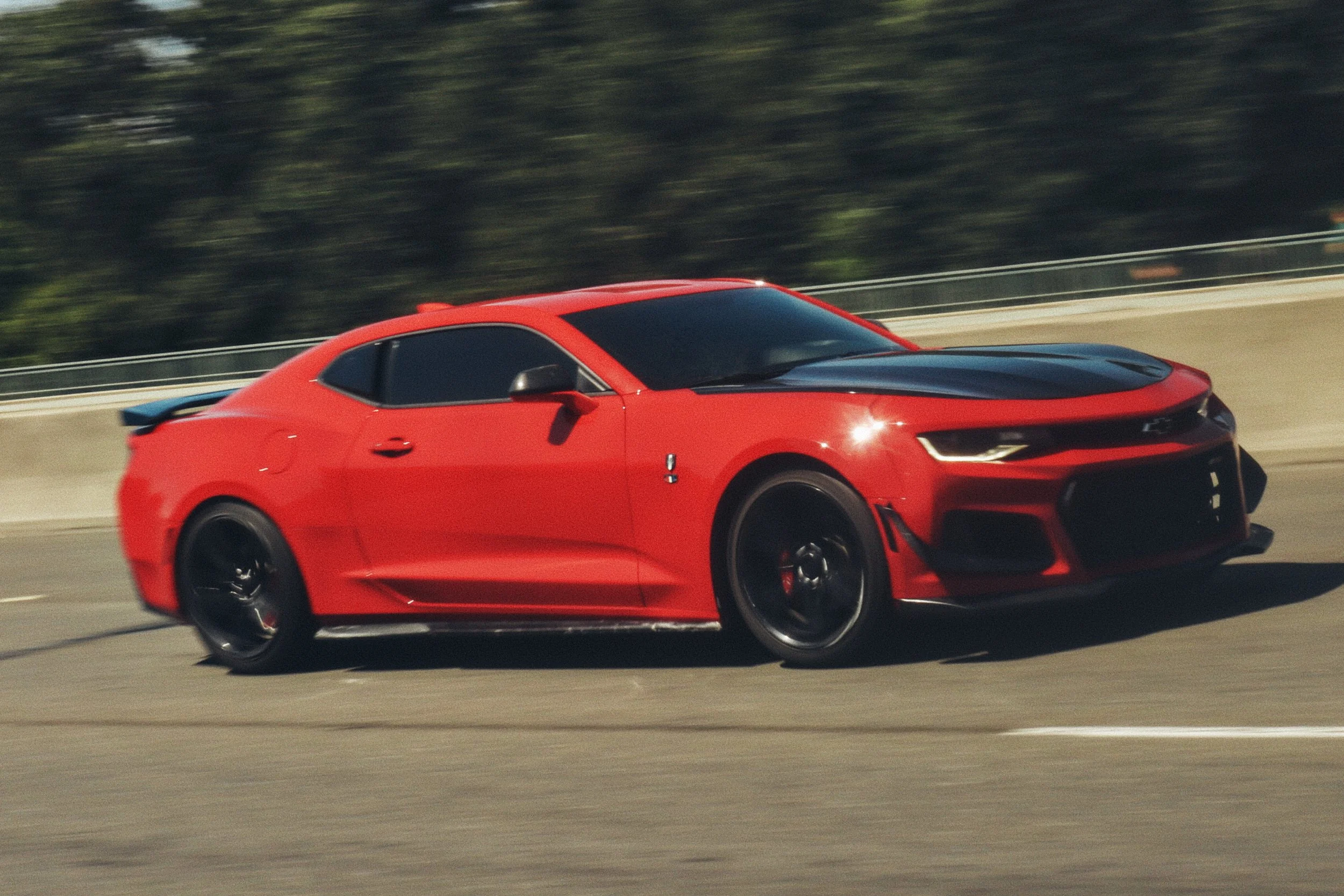 Red Chevrolet Camaro SS with black hood and wheels driving on a highway
