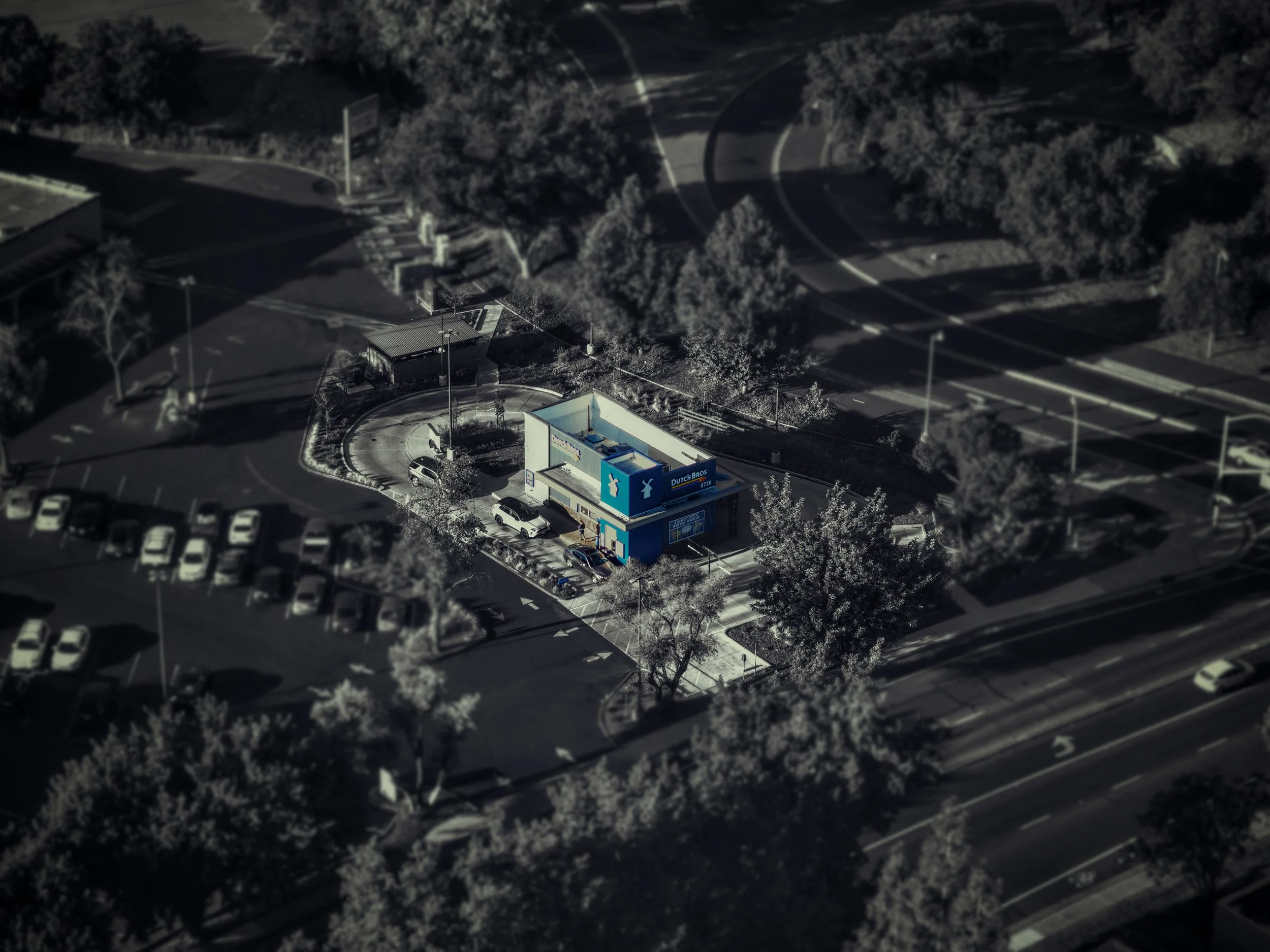A bird's eye view of a Dutch Bros coffee shop with a parking lot, trees, and surrounding roads in an urban area.
