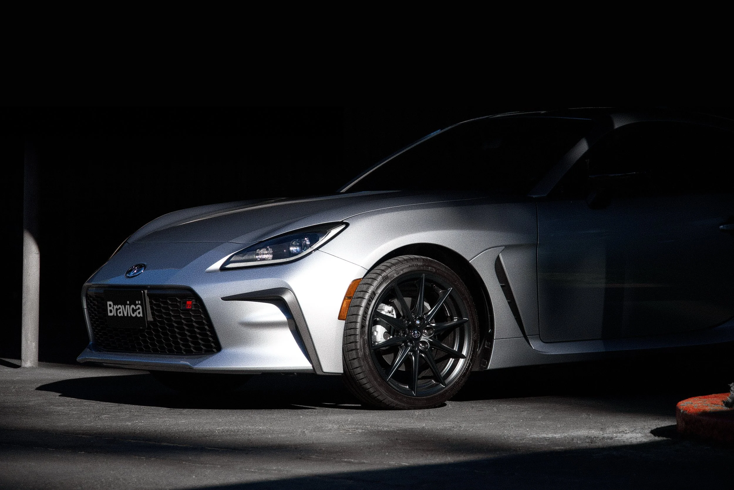 A silver Toyota sports car with black wheels parked in a dimly lit area at night.