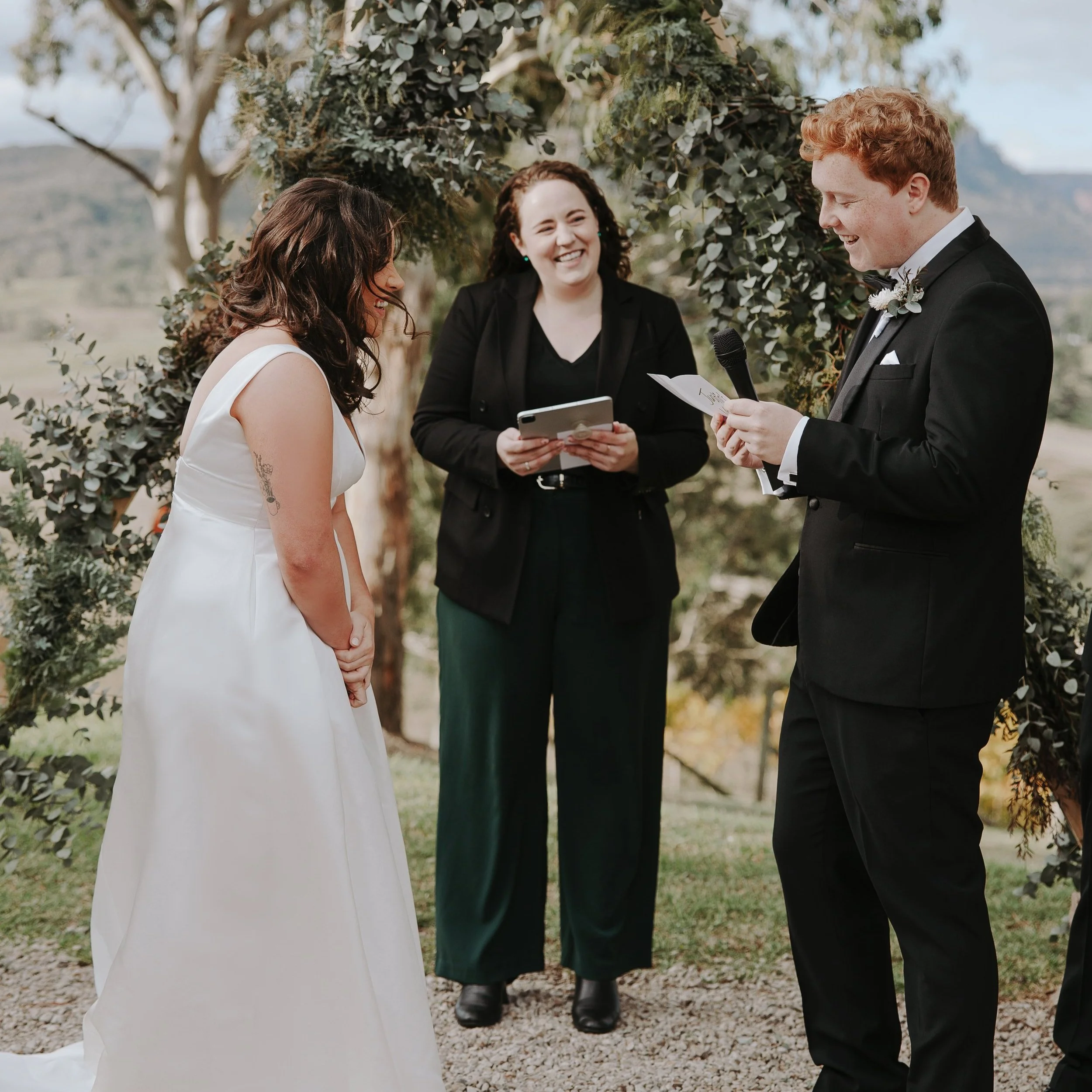 A couple getting married at Dryridge Estate winery in the Megalong Valley, with Elle the celebrant standing between them and smiling.