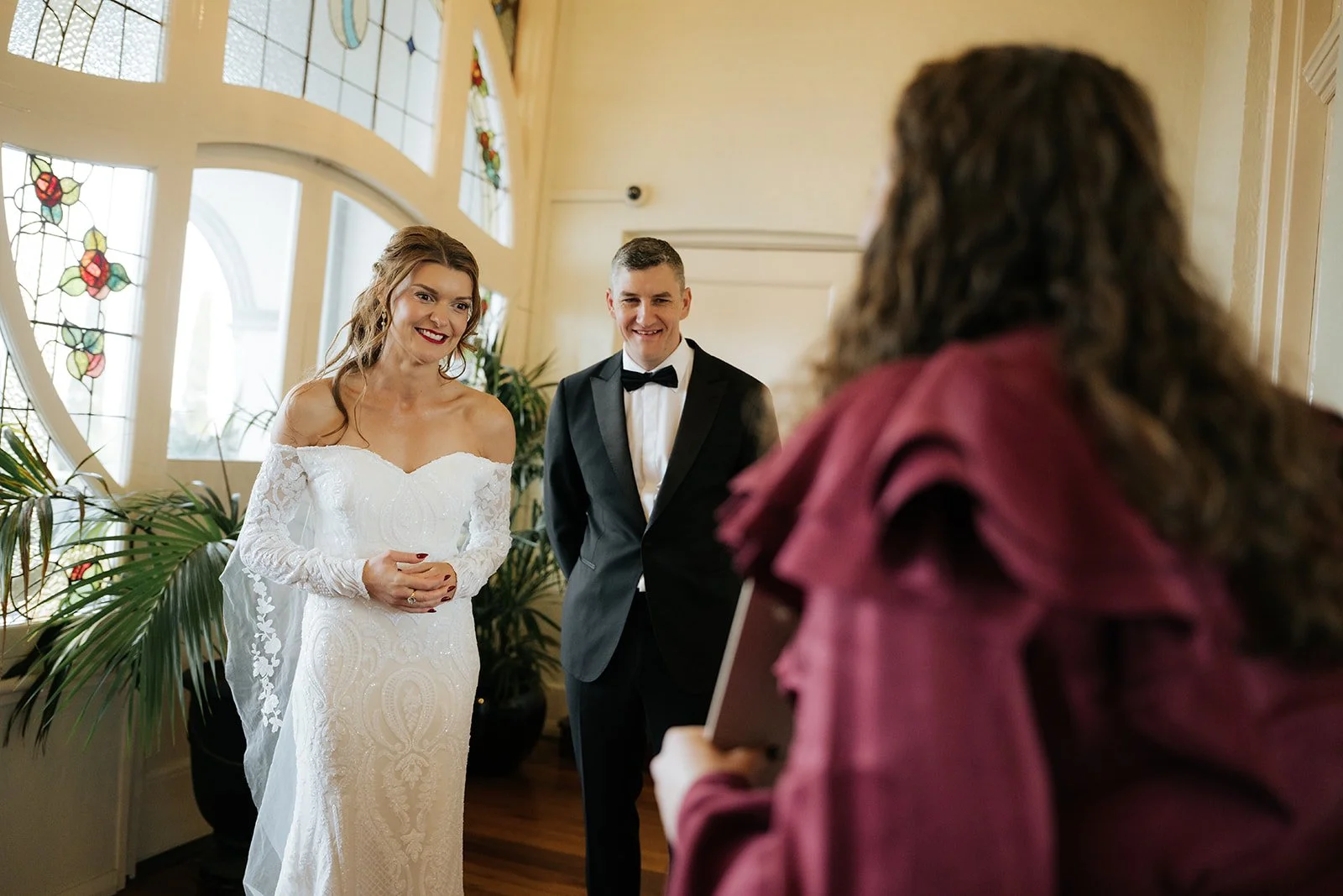 Elle the celebrant is wearing a red dress with her back to the camera, and is showing a smiling couple in their black and white wedding attire their custom kinship certificate