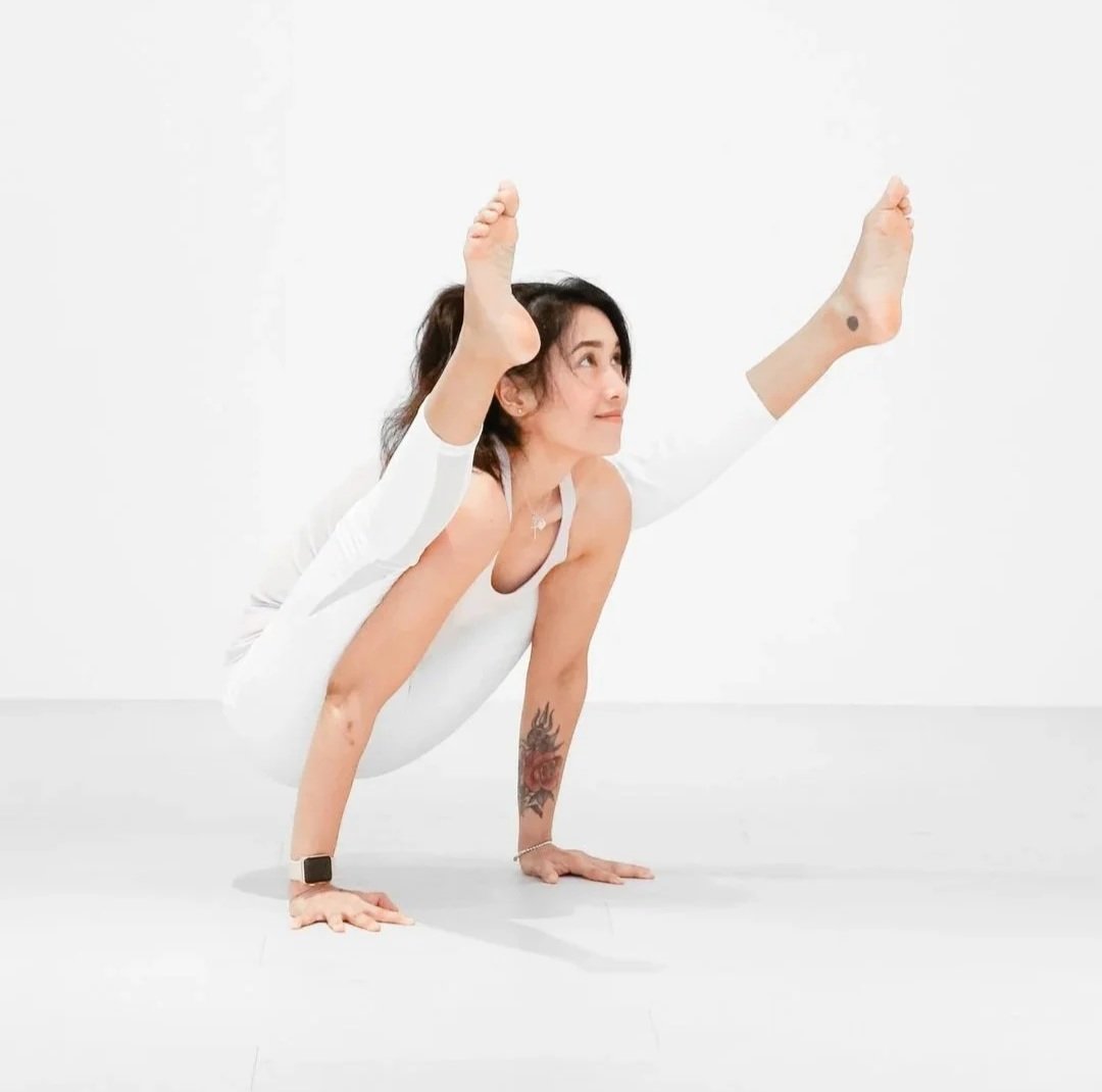 Woman in white clothing performing a yoga pose in a handstand split position against a plain white background.