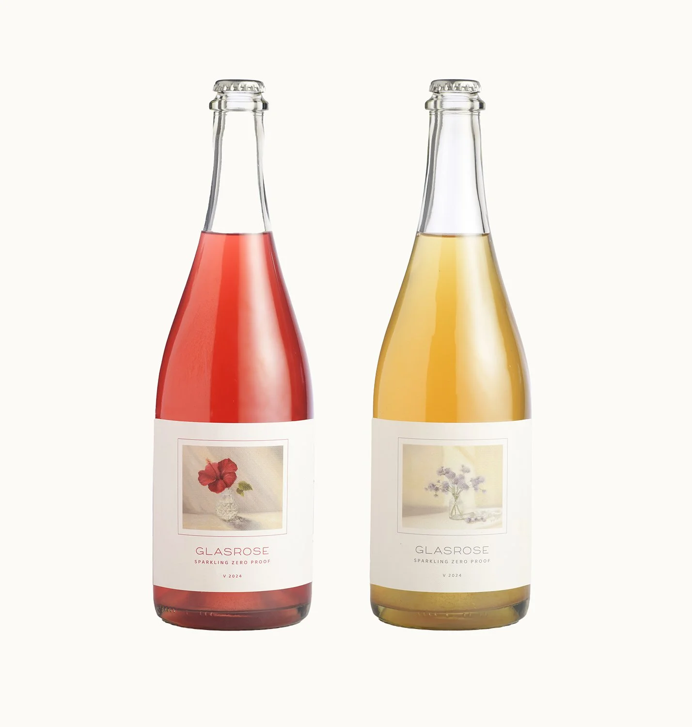 Two glass bottles of sparkling non-alcoholic drinks with floral labels, one red and the other yellow, against a white background.