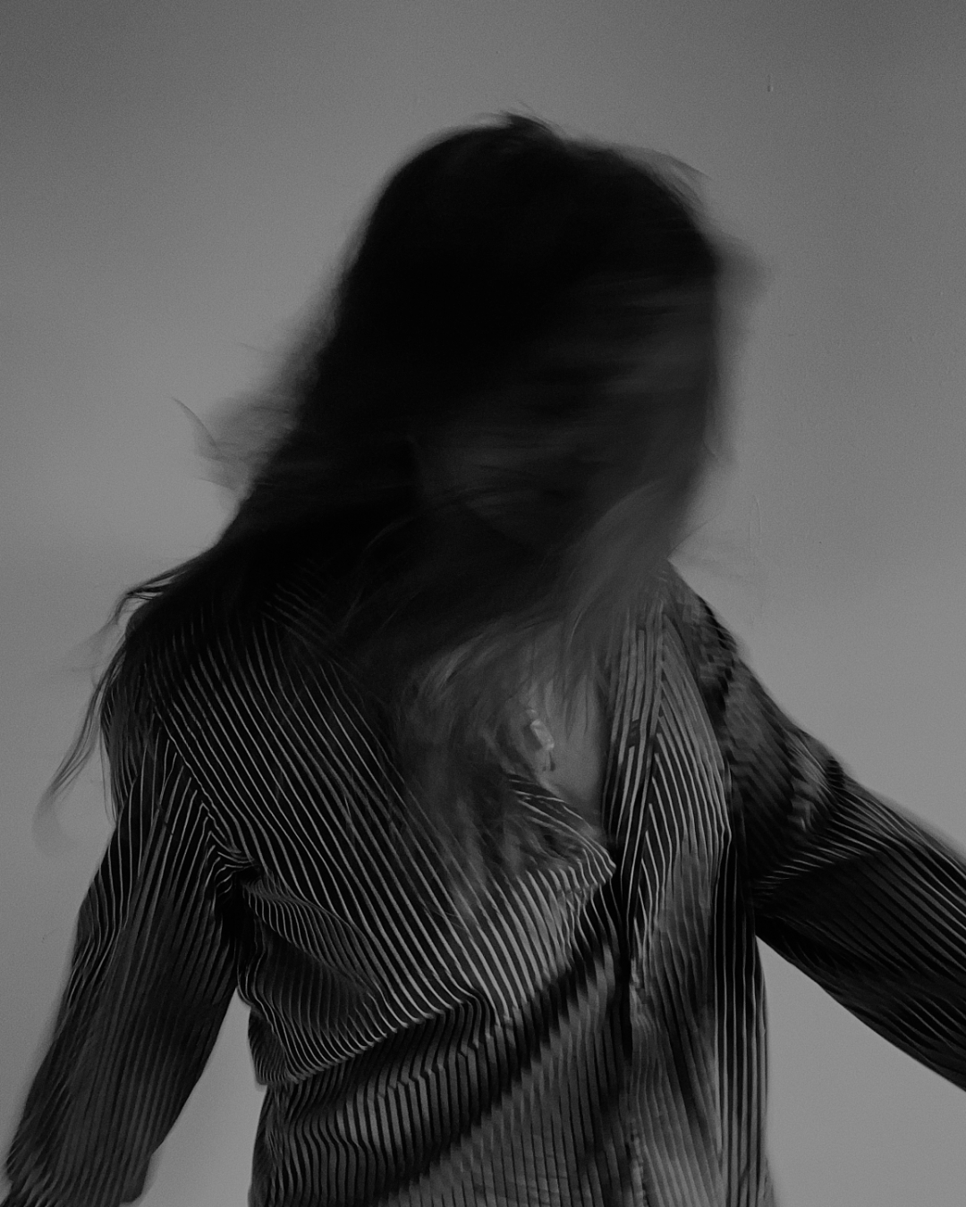 A black and white photograph of a woman with long hair, turned away from the camera, wearing a striped shirt.